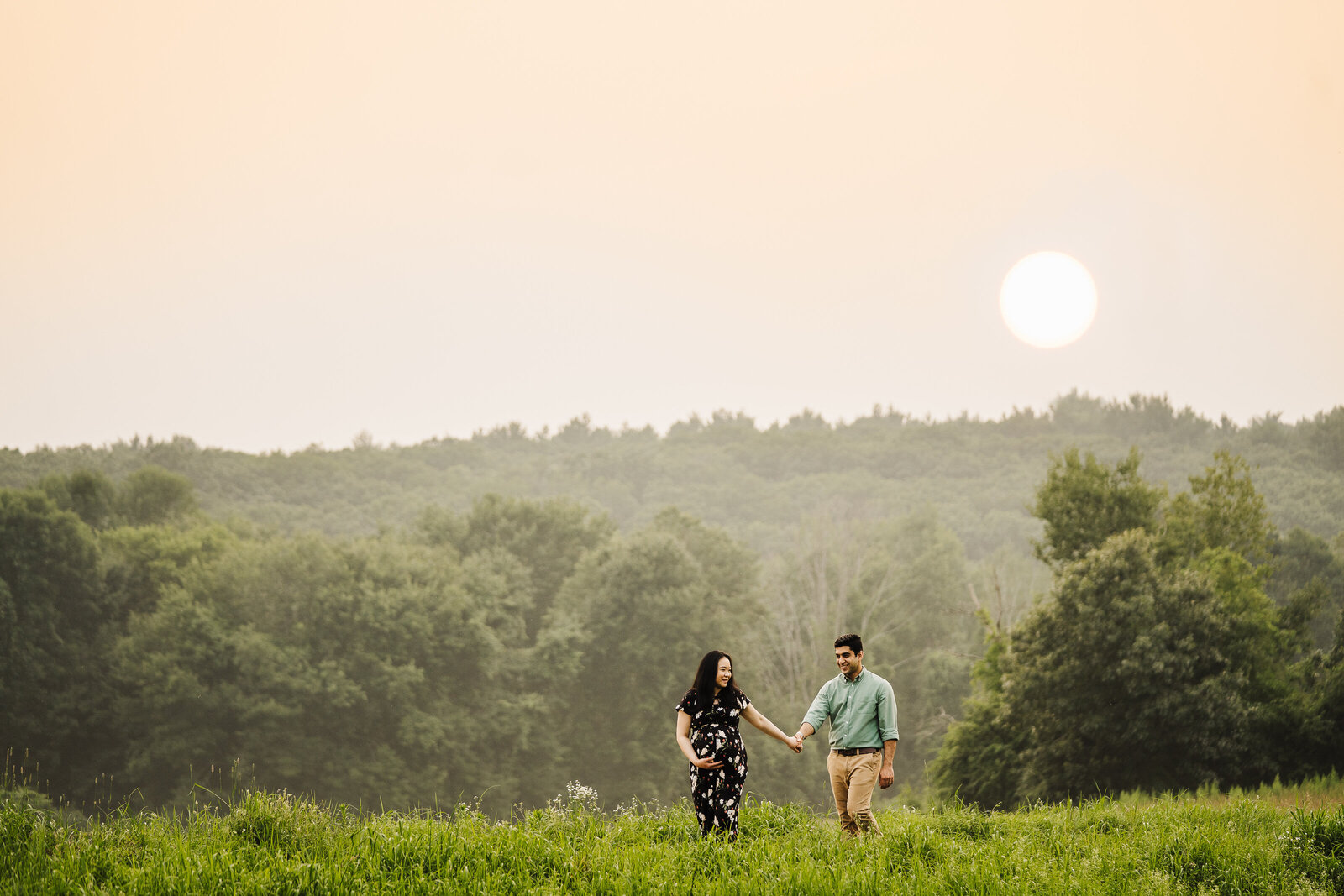 pregnant couple holding hands walks through field