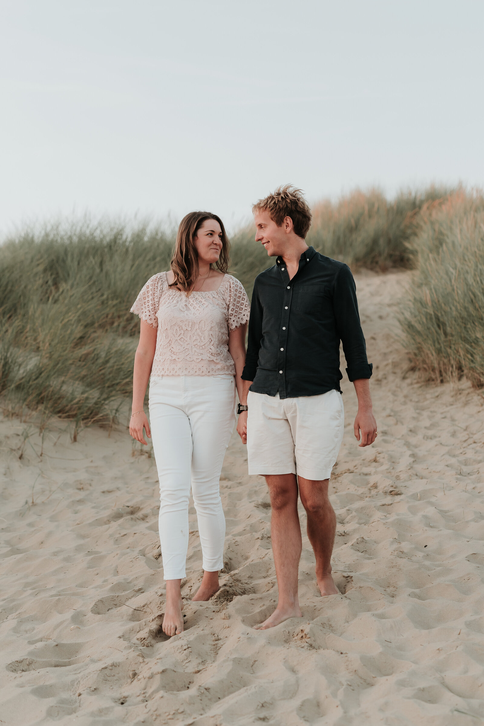Couple walking holding hands along sand dune at Camber sands beach
