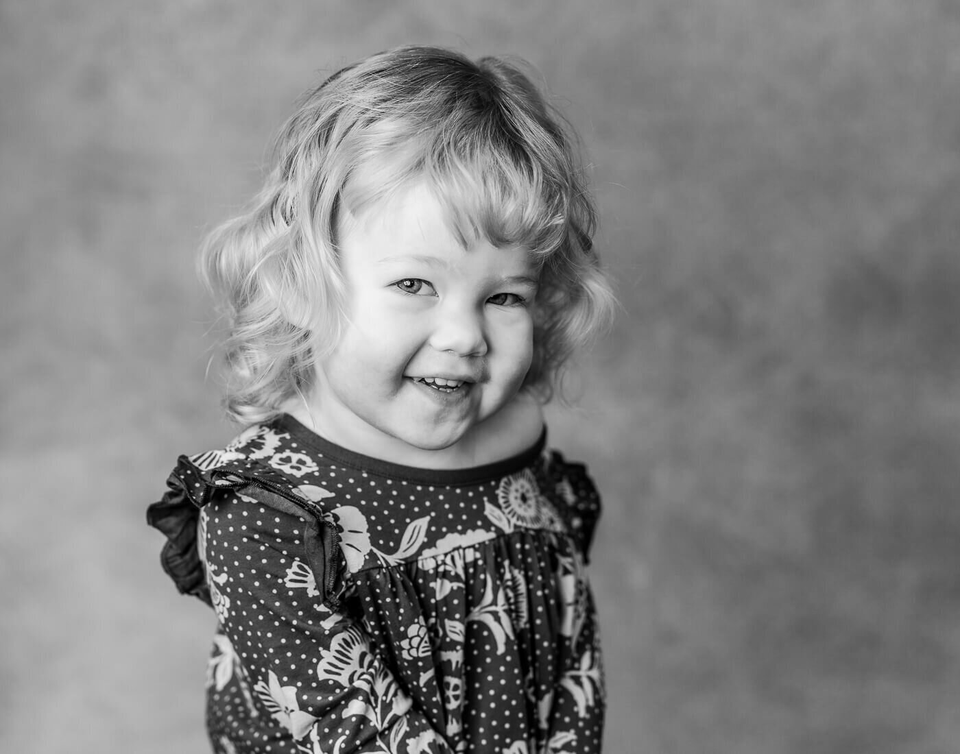 A child smiles in front of a grey background.