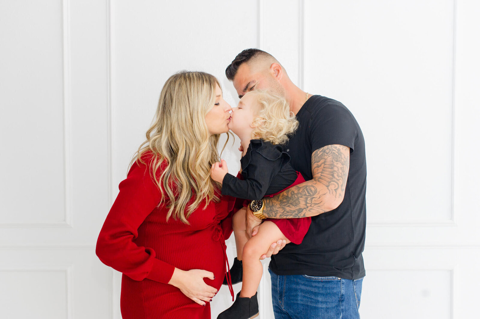 Maternity images of pregnant mother and daughter sharing a kiss while dad holds the little girl