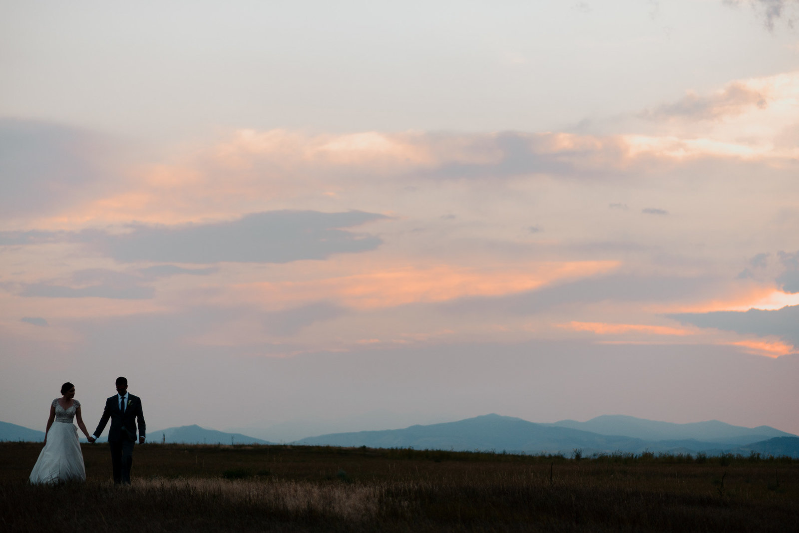 photo of newlyweds at sunset holding hands with Denver Mountains in the background.