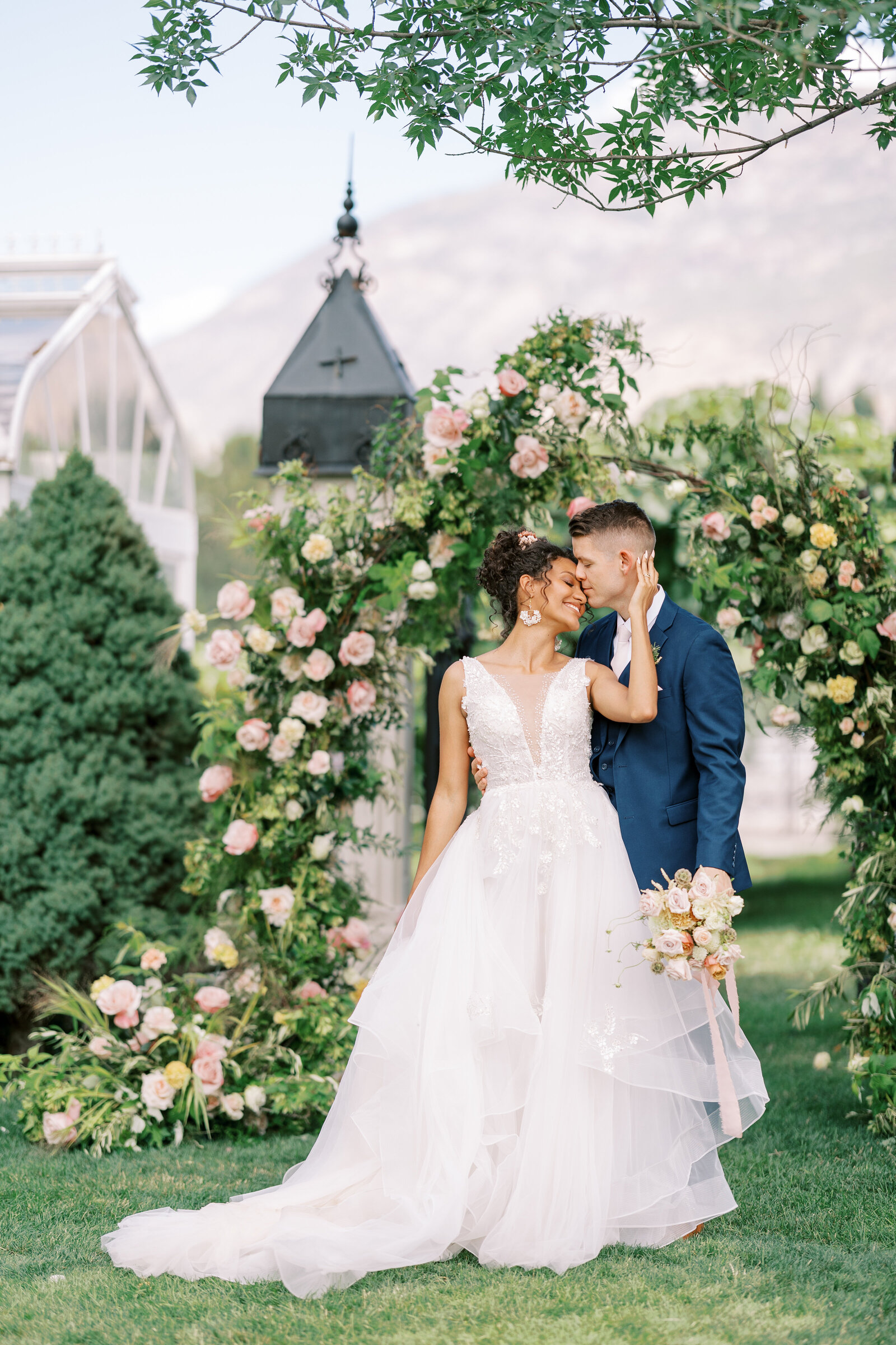 Bride and groom stand in front of floral arch with peach, pink, and white florals at Wadley Farms in Utah