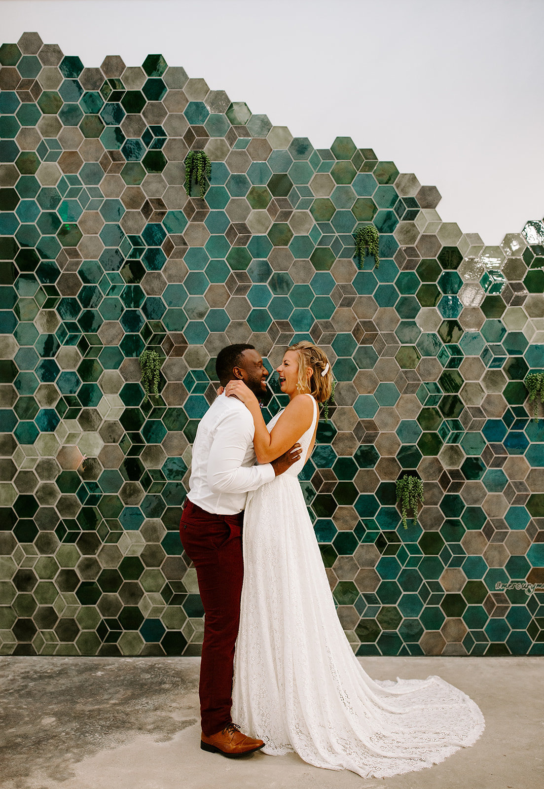 Bride and groom laughing together in front of a blue tiled wall during their Pinewood Wedding in Minnesota