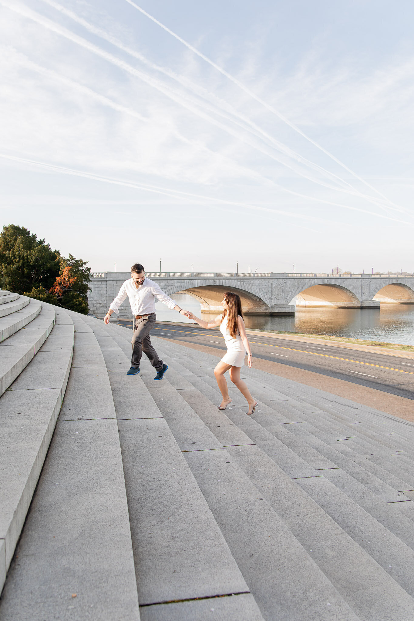 A man holds the hand of his fiancé as they run up a large staircase in Washington D.C. 