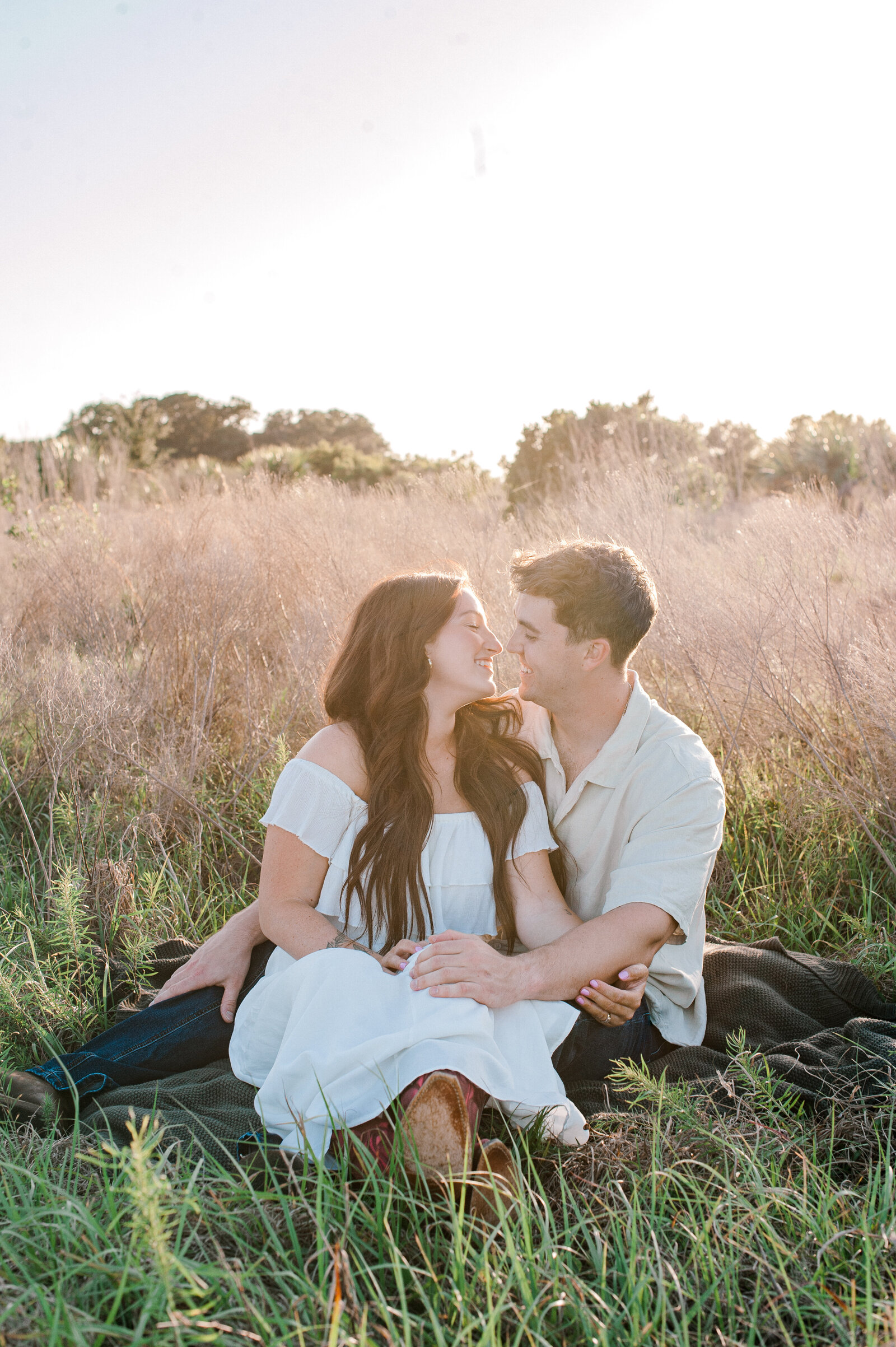 Orlando couples photographer captures a couple sitting in a tall grass field going in for a loving kiss at sunset
