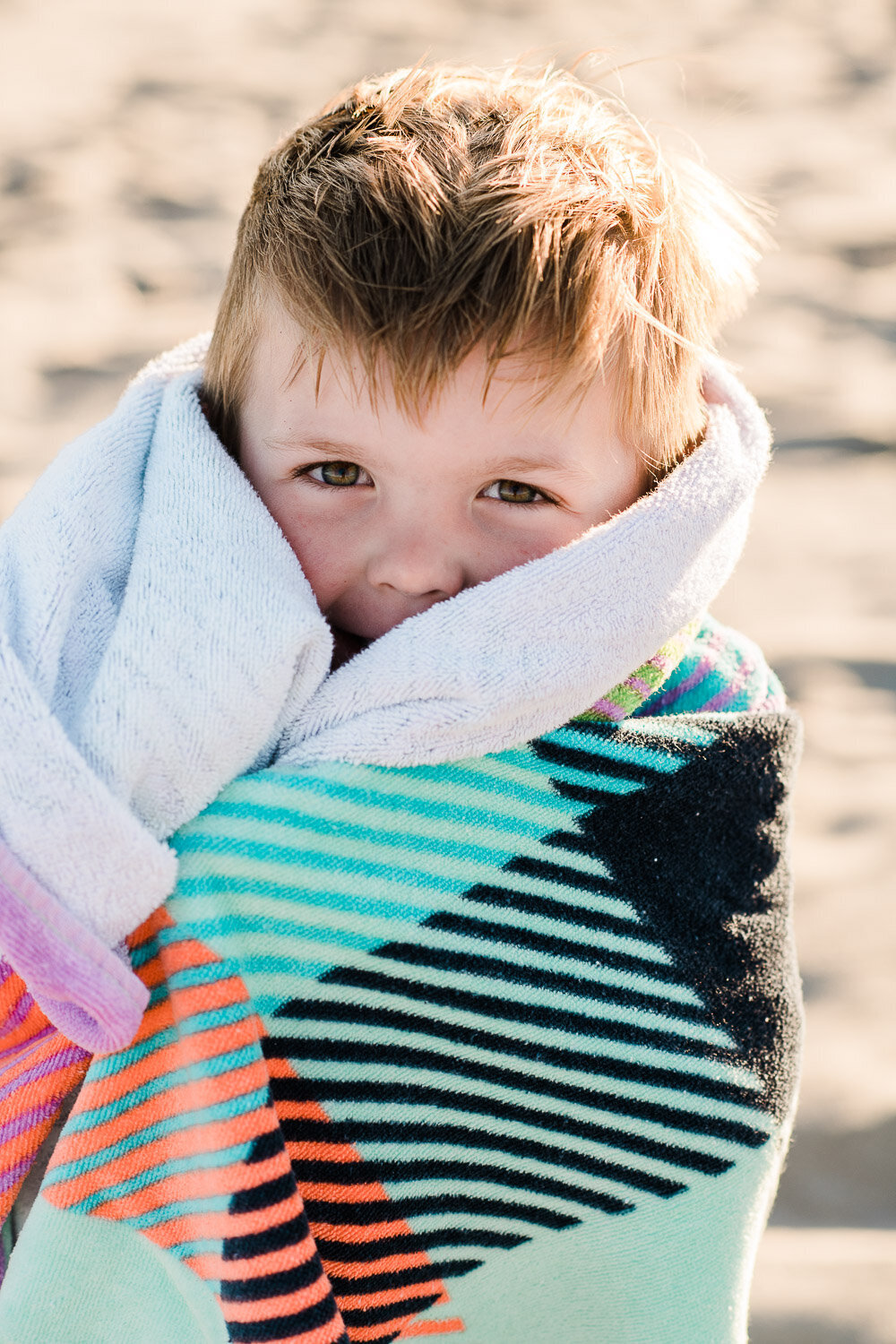 toddler boy wrapped in towel on beach