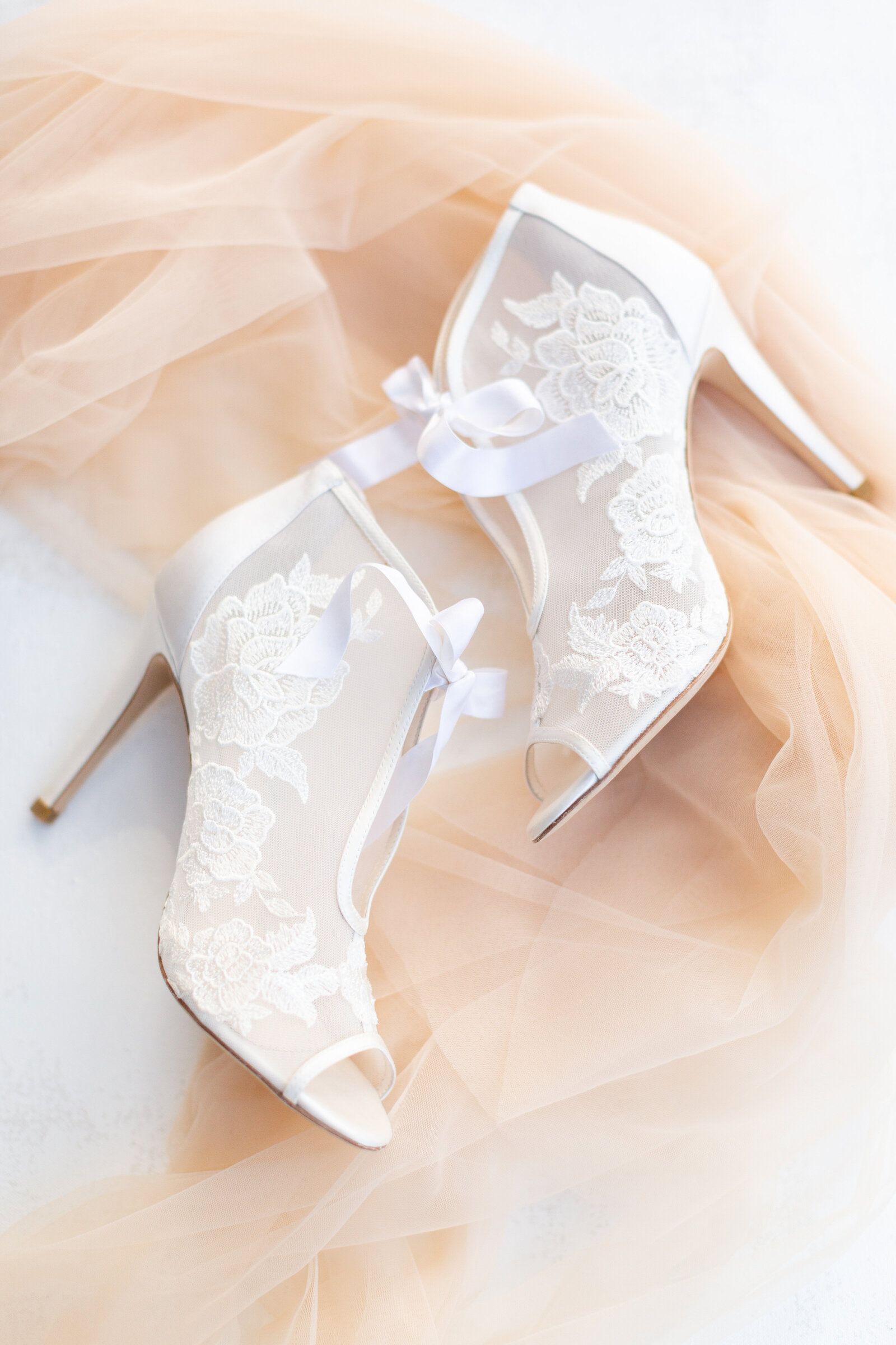 Two white heels laid on top of a veil.