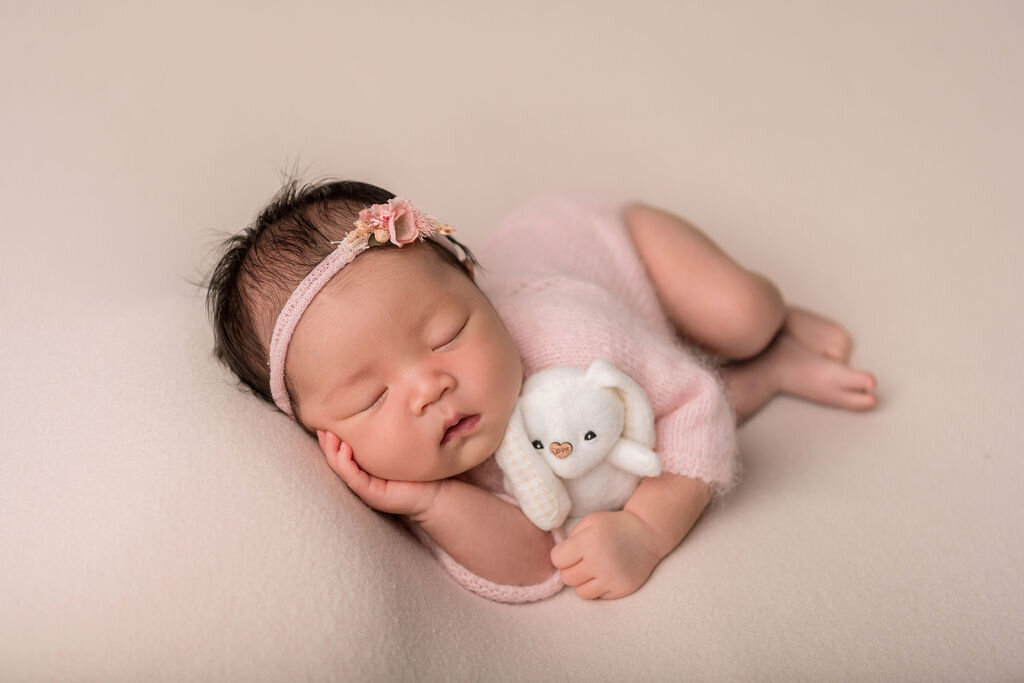 Connecticut newborn photographer captures baby girl in pink wrap holding tiny white teddy bear