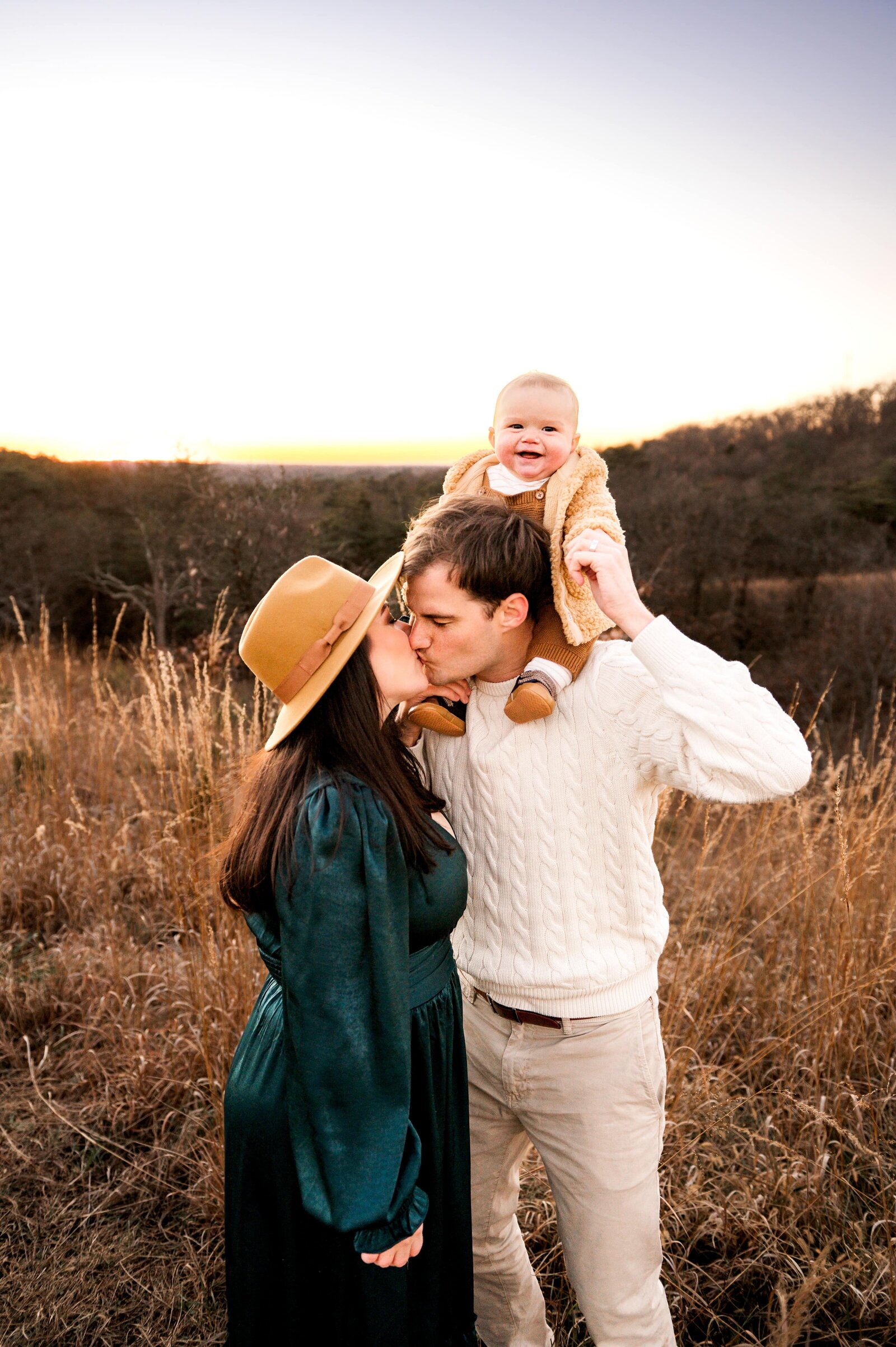 mom and dad kissing while baby is on dads shoulders