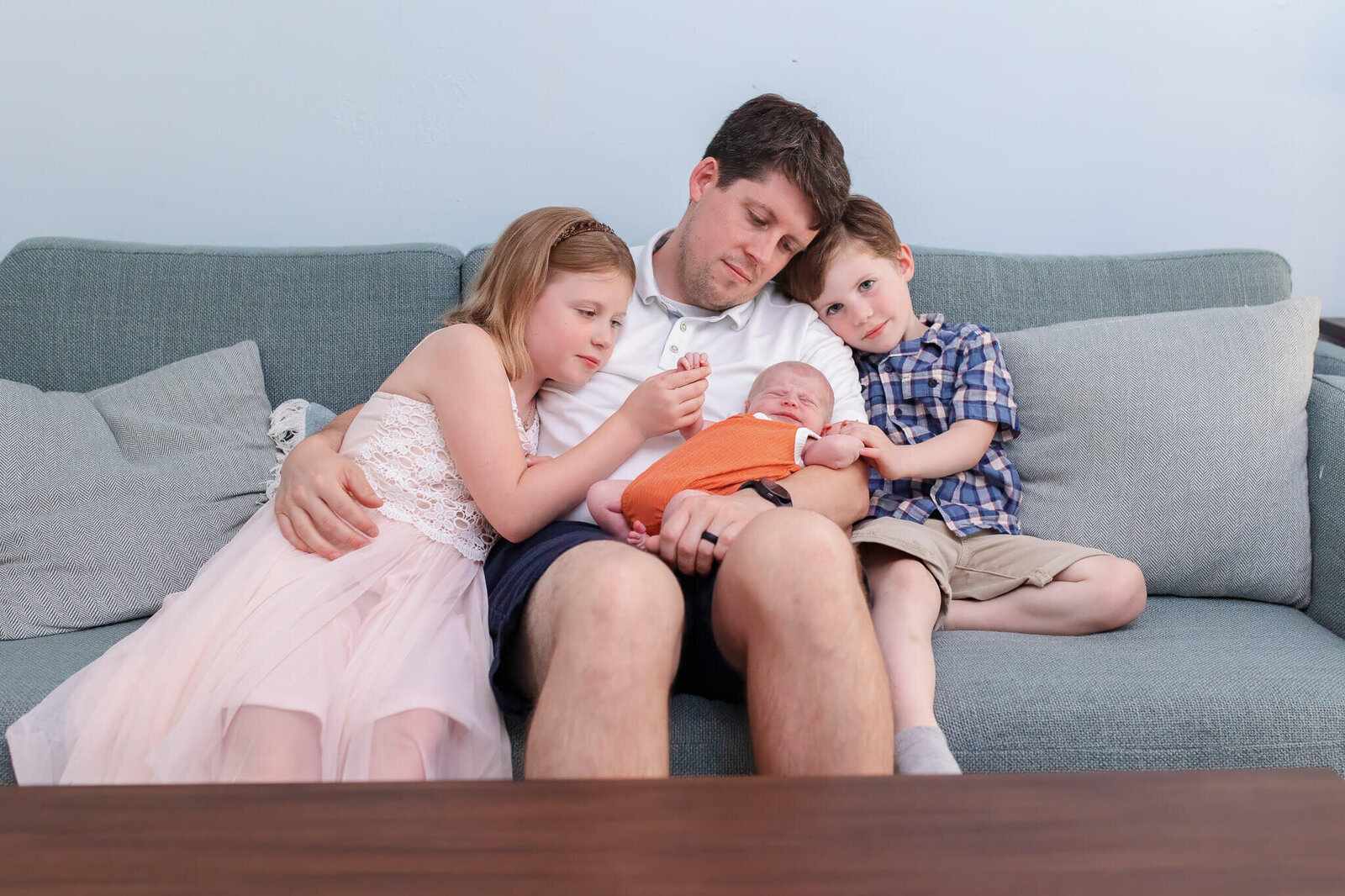 A dad with his three children sitting on the couch.