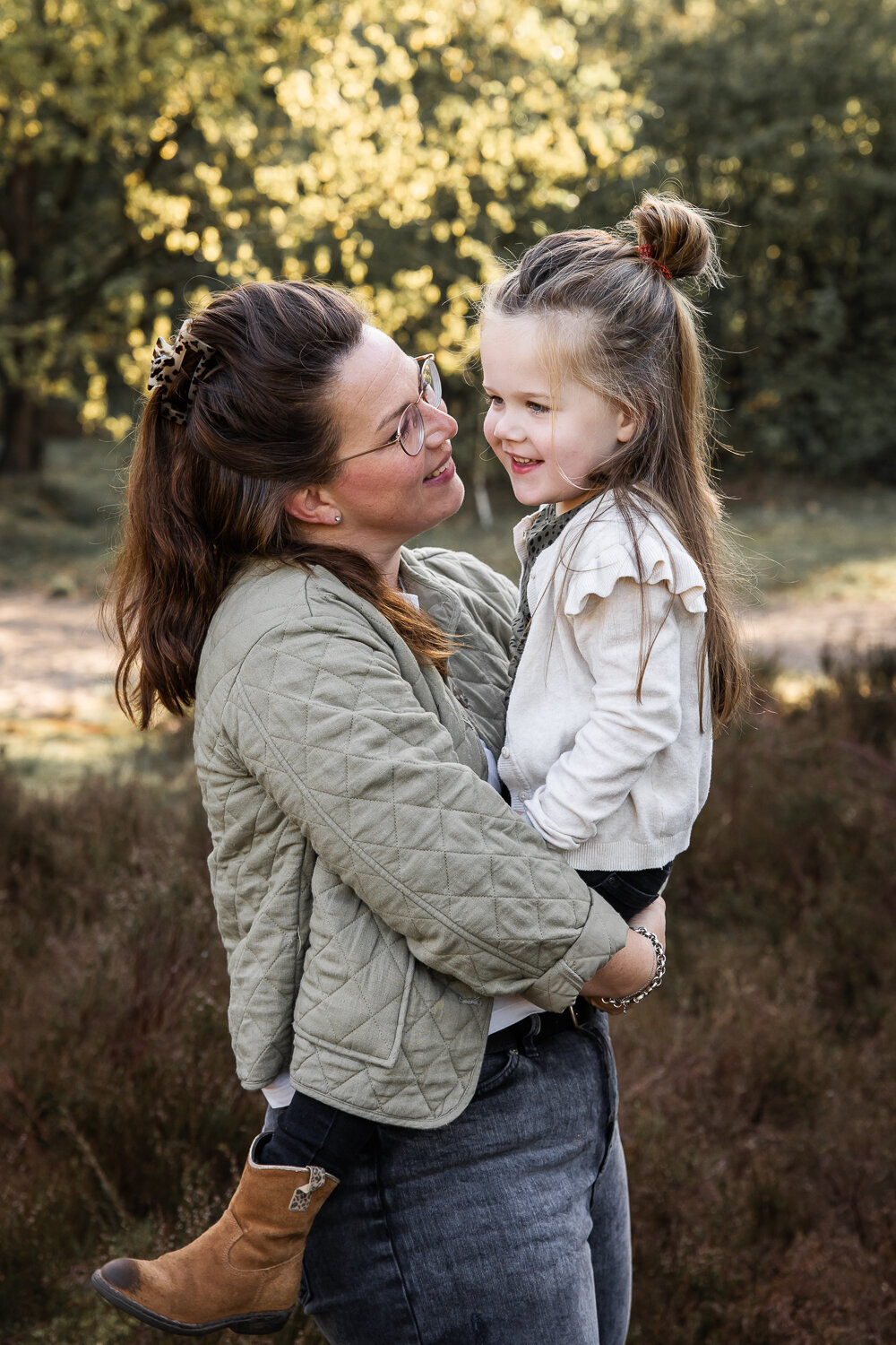 Ee moeder tilt haar dochter op en kijkt liefdevol naar haar tijdens een ontspannen gezinsshoot.
