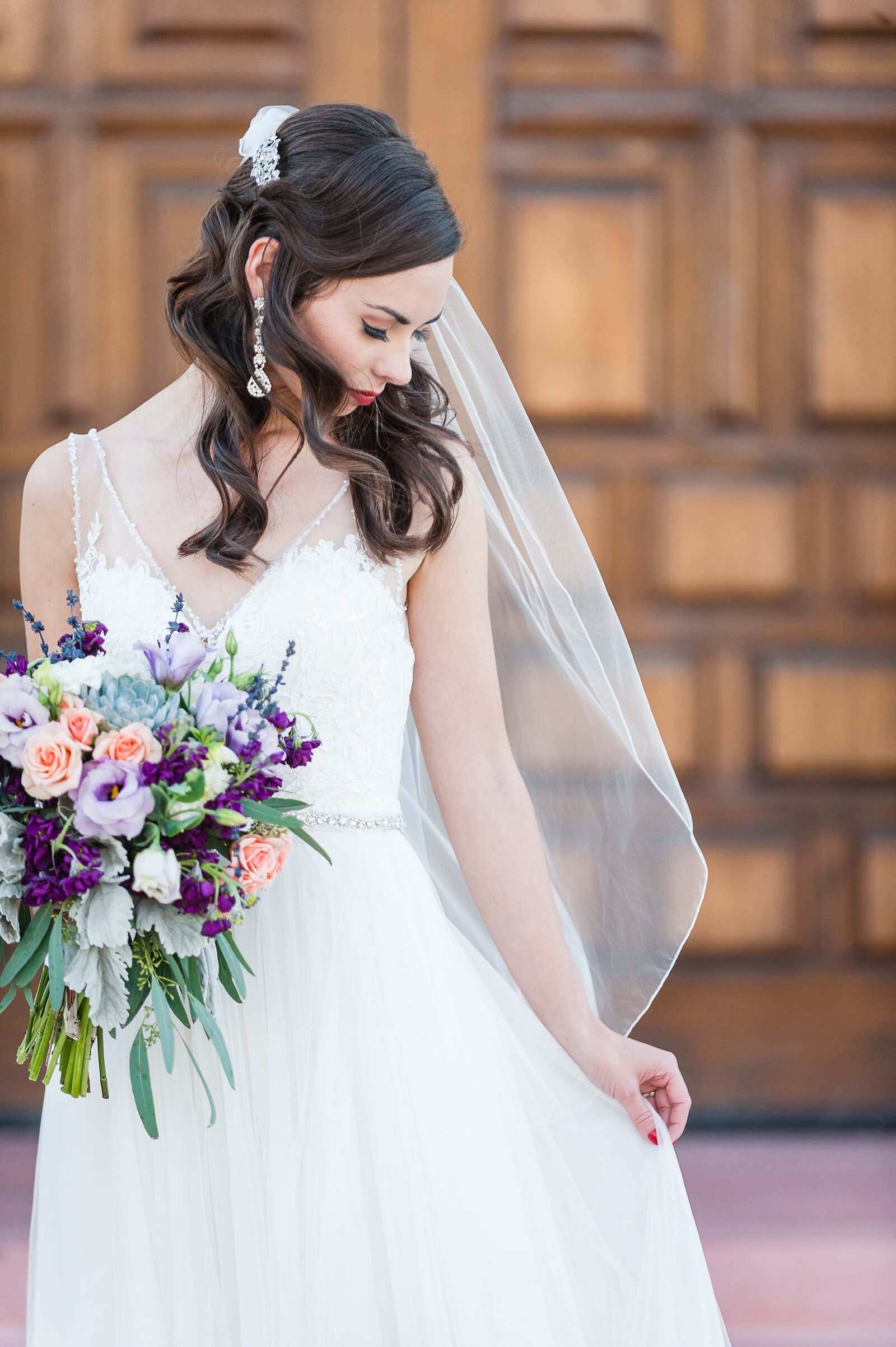Bride outside the Wigwam holding her veil and bouquet of purple and peach flowers.
