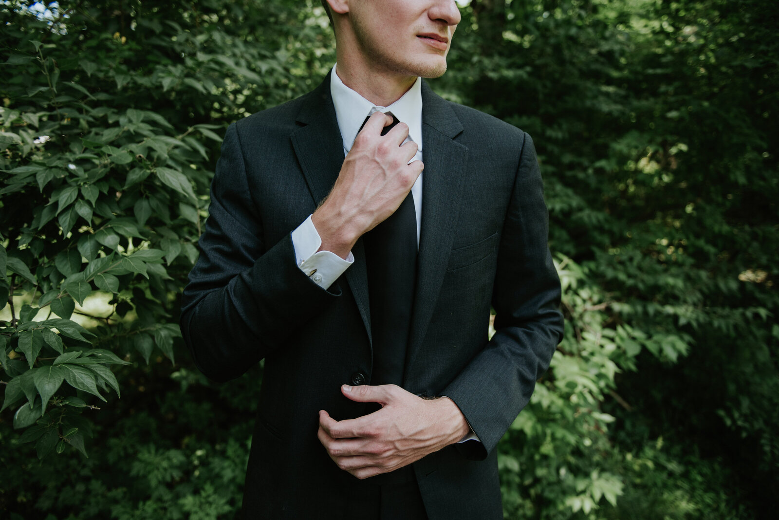 A groom adjusts his tie in the woods