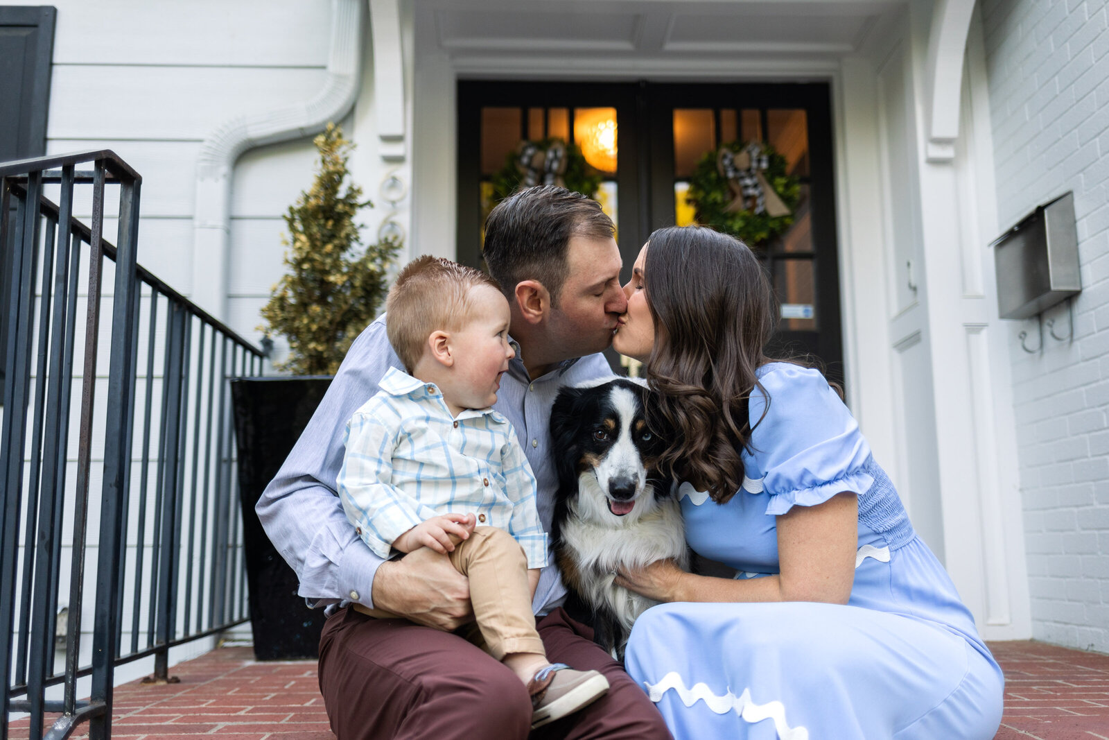 Kansas_City_Family_Photographer_mission_hills_family_on_steps_with_dog_parents_kissing_baby_smiling-65
