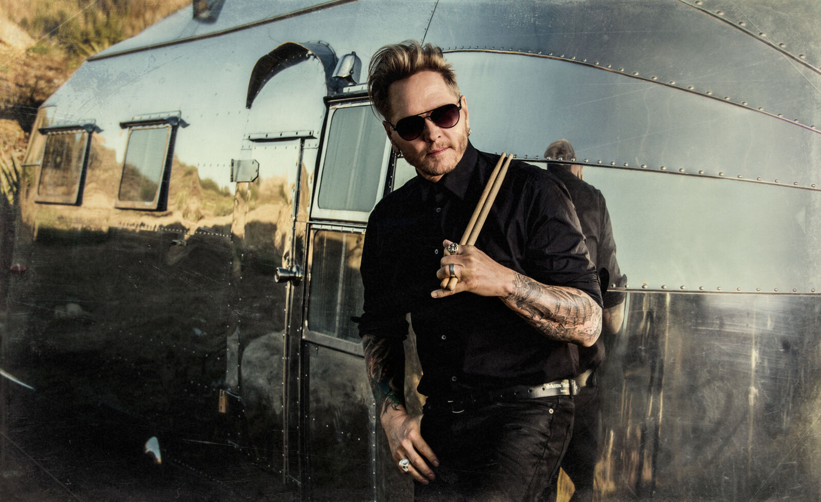 Music portrait Matt Sorum leaning against silver trailer holding drum sticks