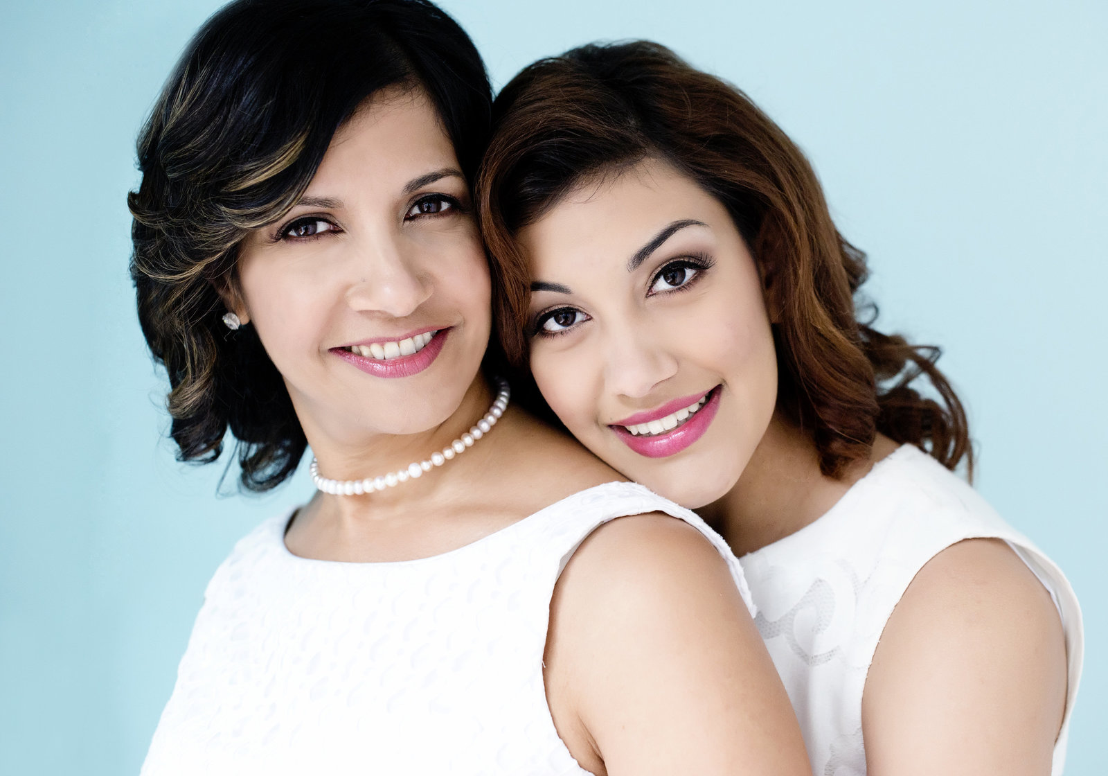 Realtor -mother and  daughter hugging and  smilling looking into camera wearing white dresses and  pearl earrings
