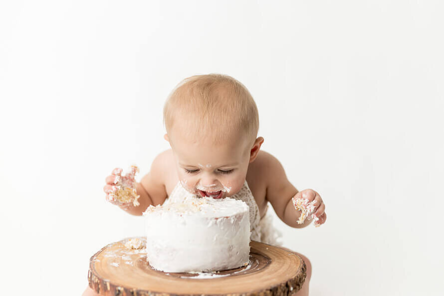 One year old eats white cake during his photo session.
