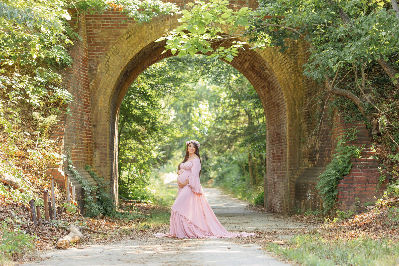 A mom-to-be in pink posing under a bridge in Lorton, VA.