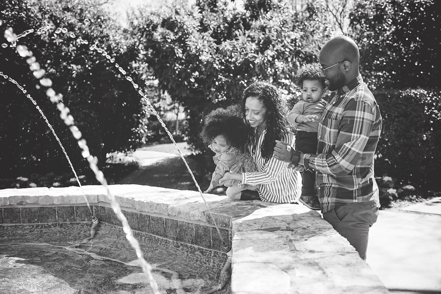 Black and white image of a family playing with water from a fountain at The Dallas Arboretum.