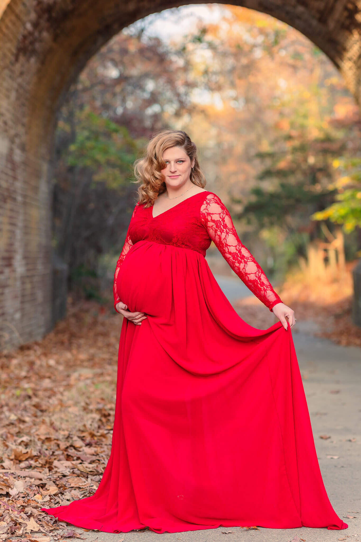 An expecting woman in a red dress posing under a bridge in Lorton, Virginia.