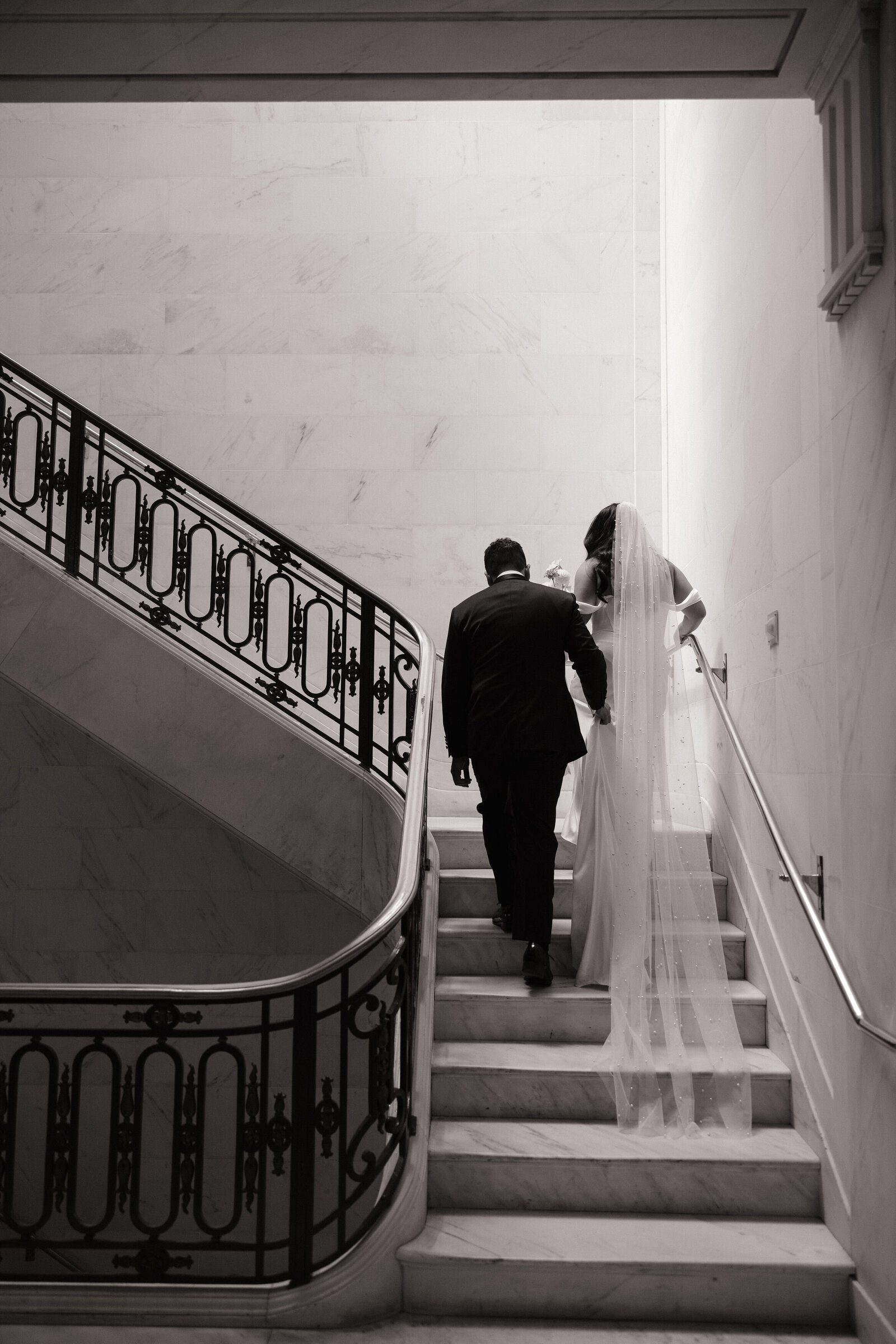 Bride and room walk up marble staircase in City Hall by Northern California wedding photographers