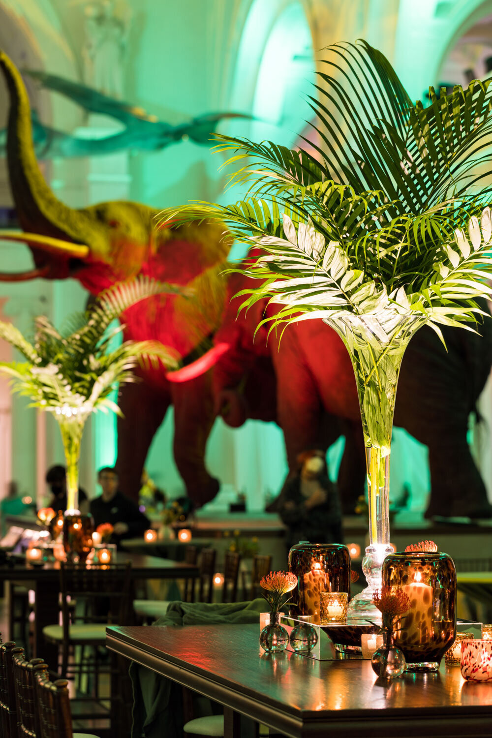 Event setup with tall palm centerpieces and elephant exhibit in the background