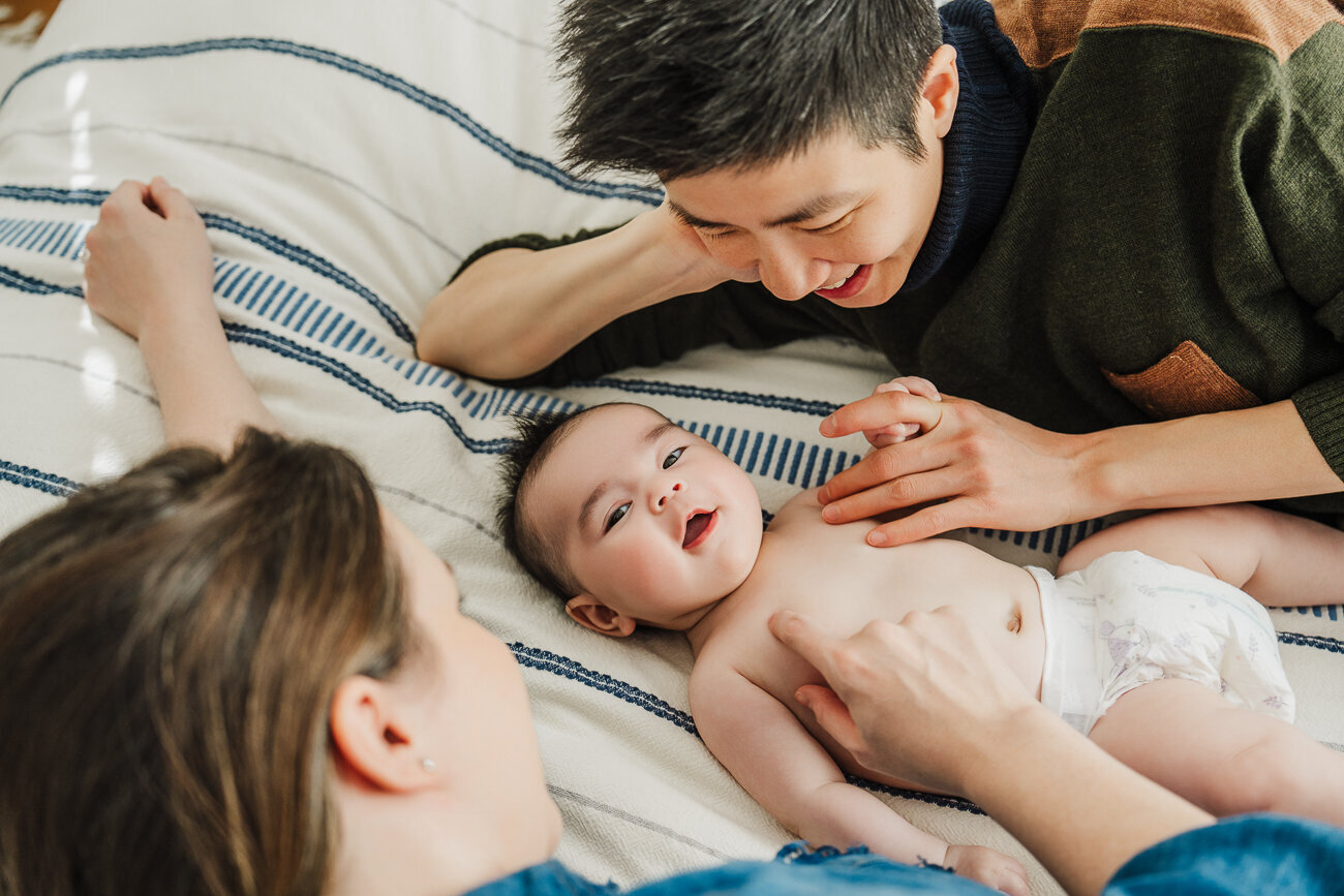 moms lean over new baby laying on bed