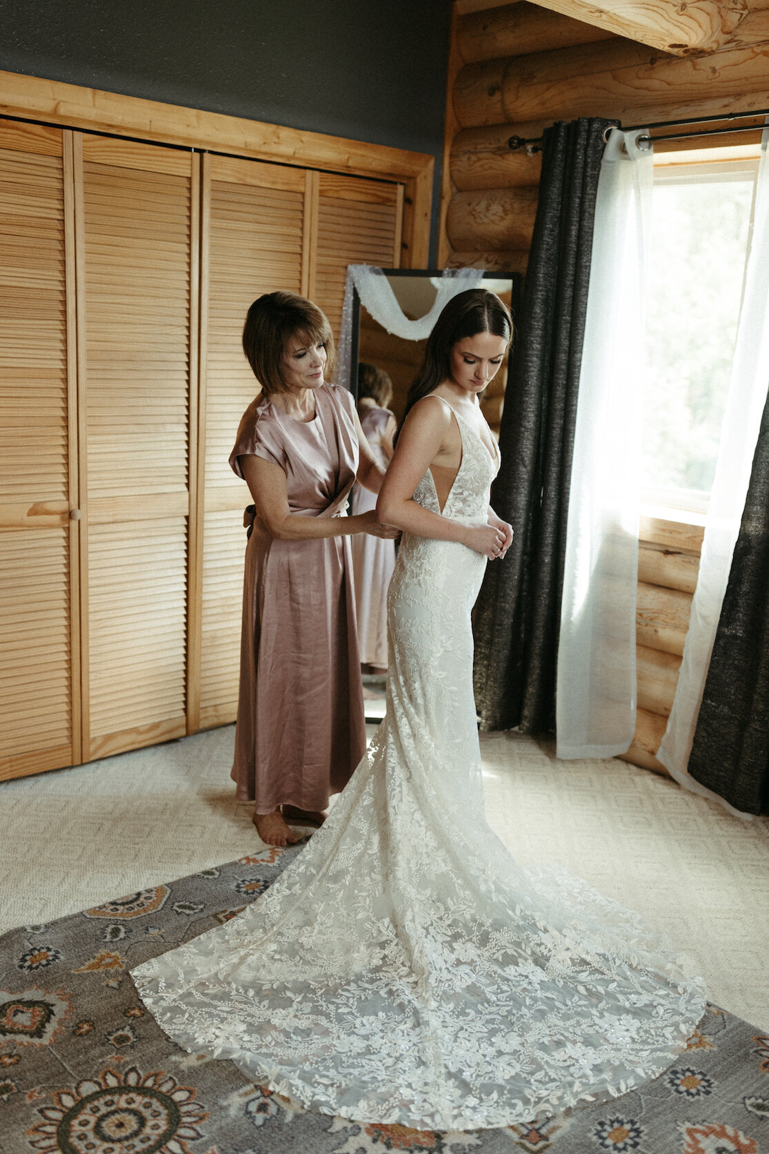 Woman helping her daughter put on  her wedding dress