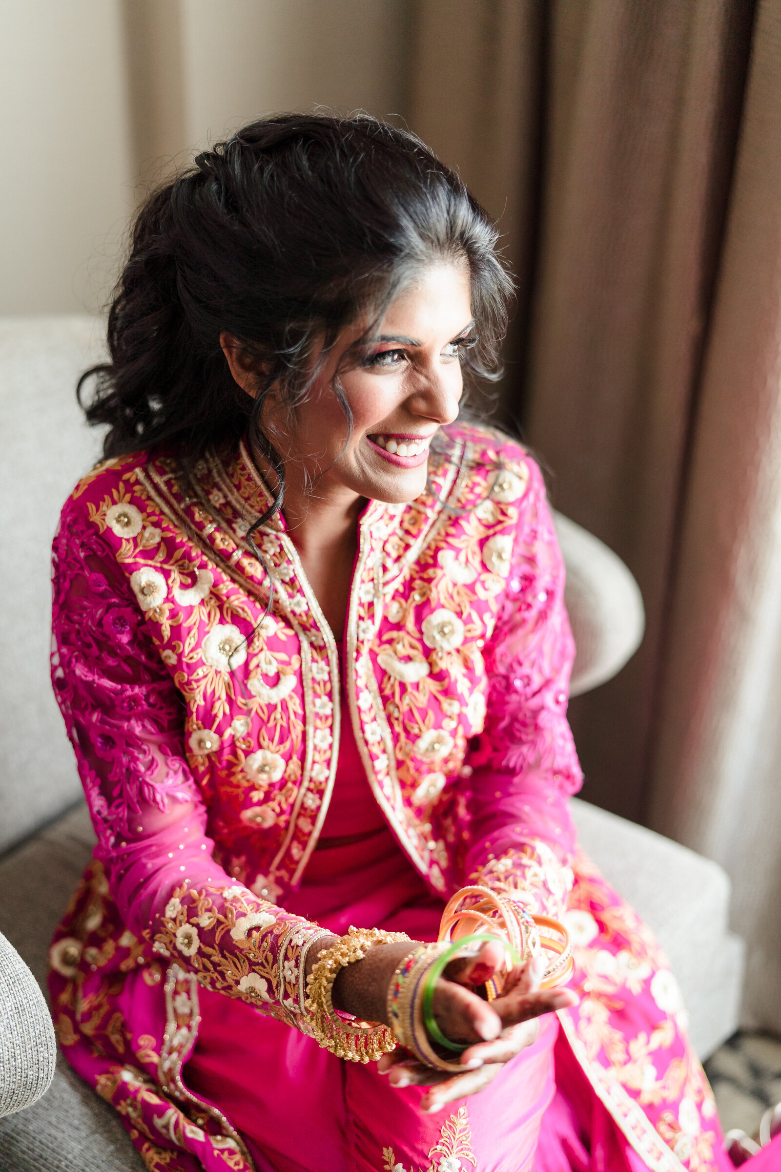 A bride in a pink lehenga smiles as she prepares her details
