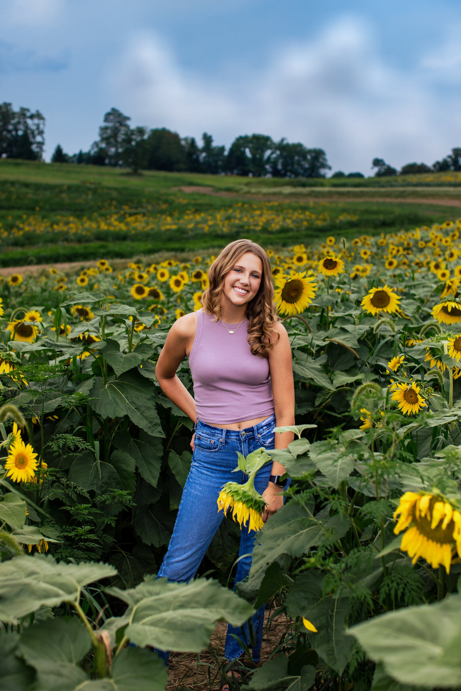Smiles and turns in a sunflower field wearing blue jeans and a bright pink shirt she smiles off into the distance.