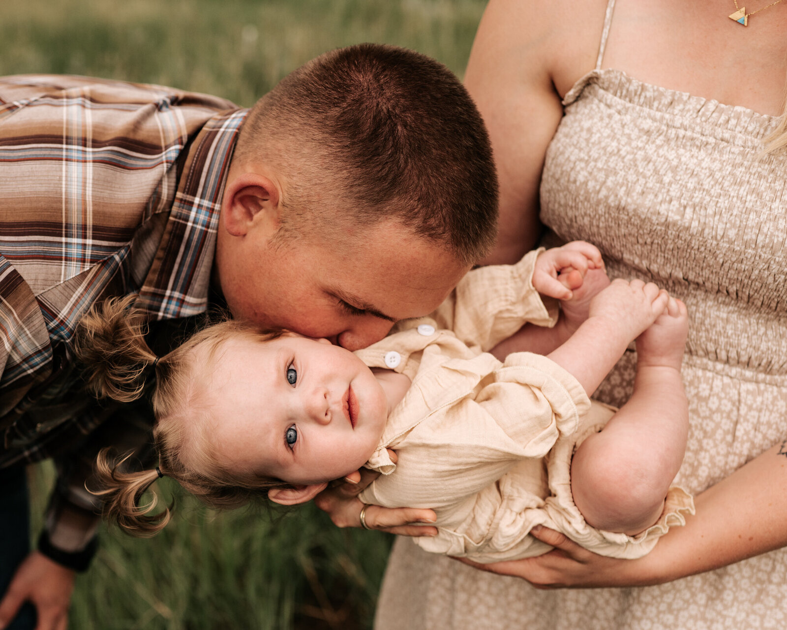 Mom tilting daughter towards dad while dad kisses his daughter on the cheek