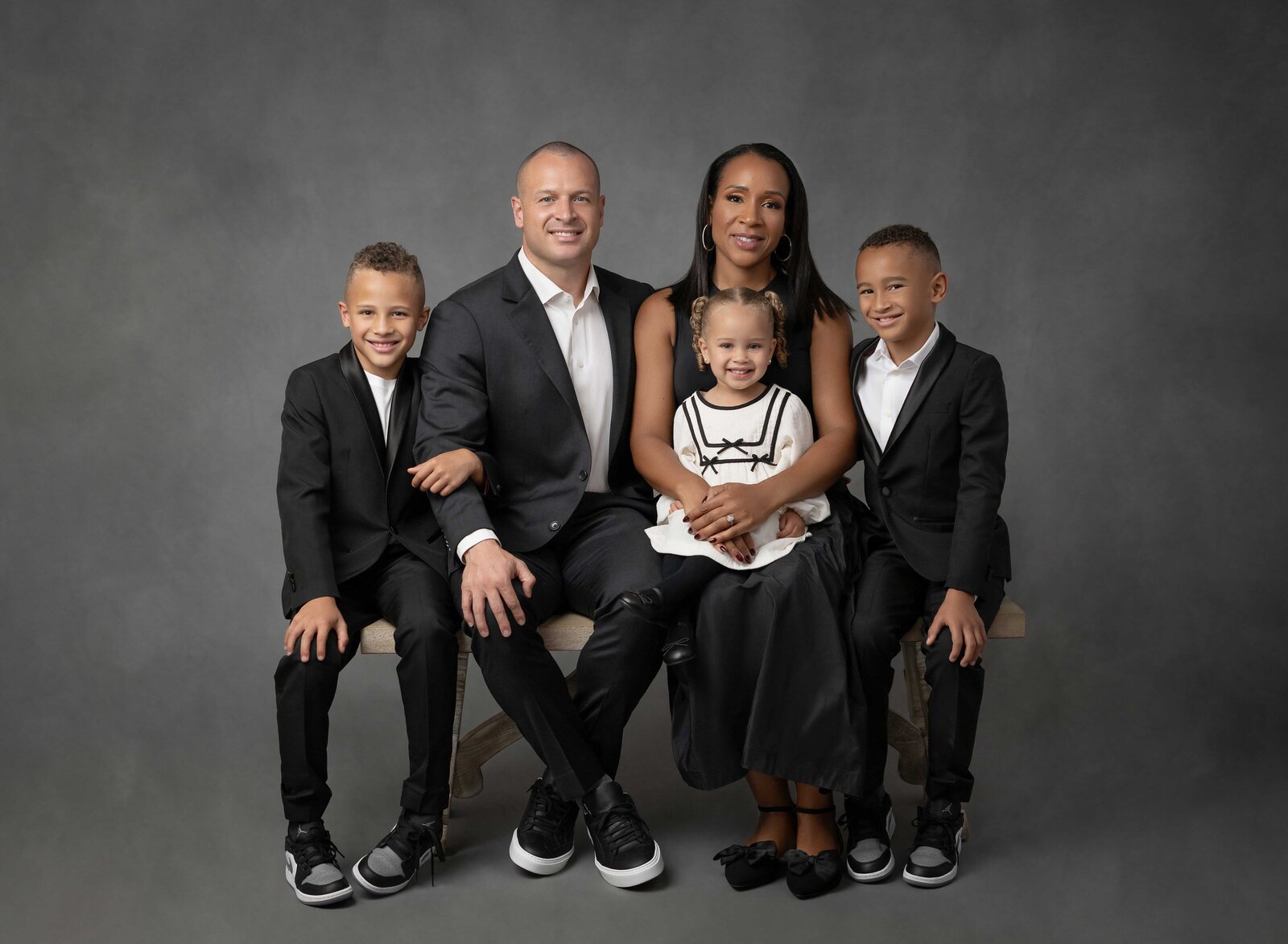 Family of 5, dressed in black, sitting on bench and smiling at camera. Family photo taken at Atlanta Photo Studio by Jenni Nikki Photography.