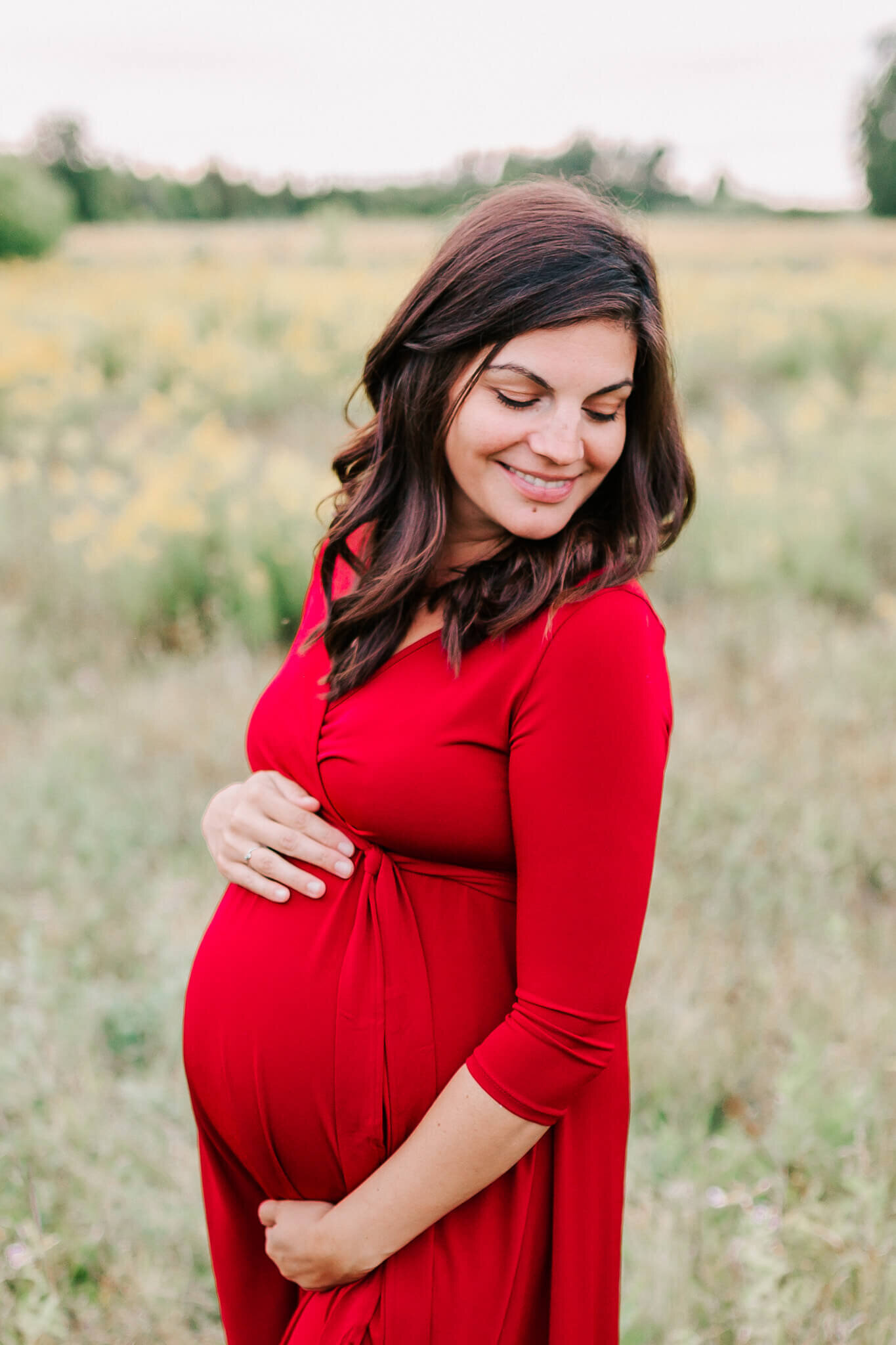 Mother in red smiles over her shoulder during her maternity session.
