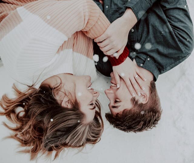 couple laying in the snow together for their winter engagement session in Idaho