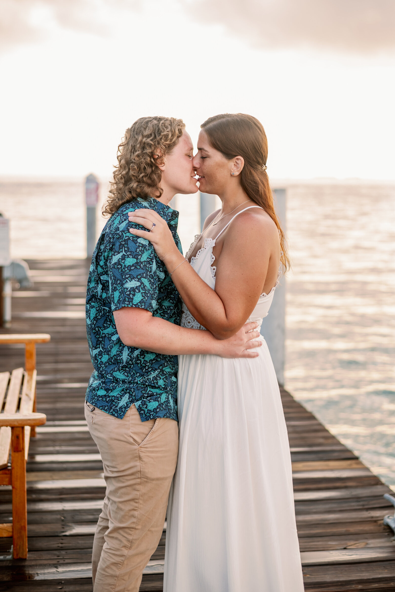 LGBTQ engaged couple standing on a dock during sunset in an embrace and about to kiss