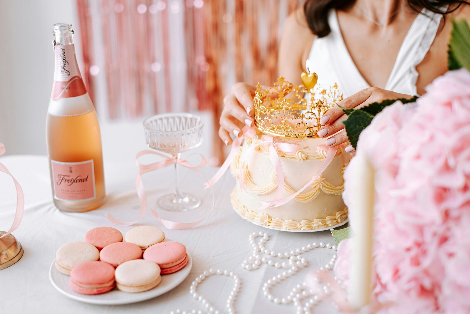 Pink and gold party table with cake, crown topper, macarons, and champagne