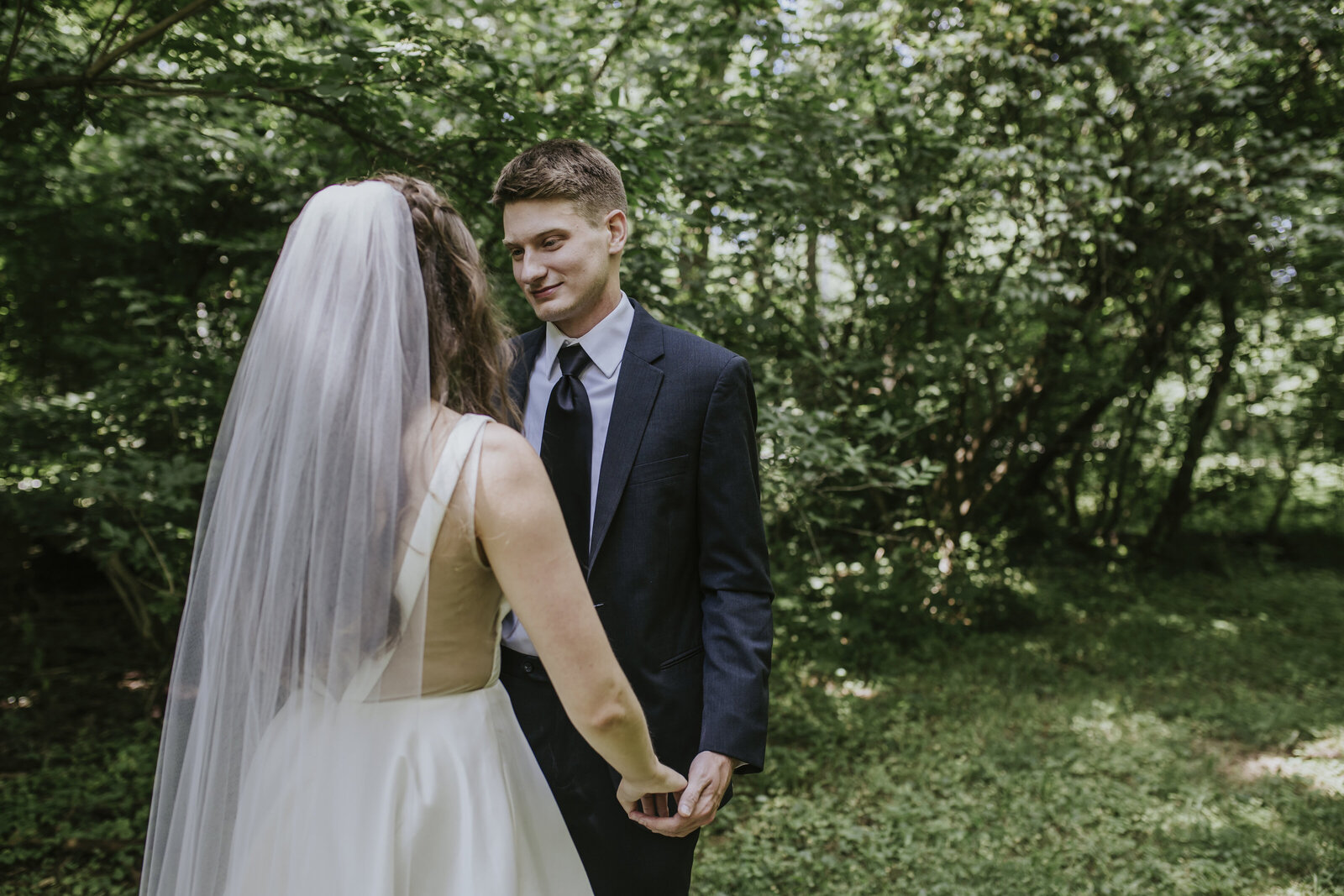 A groom smiles at a bride in the woods