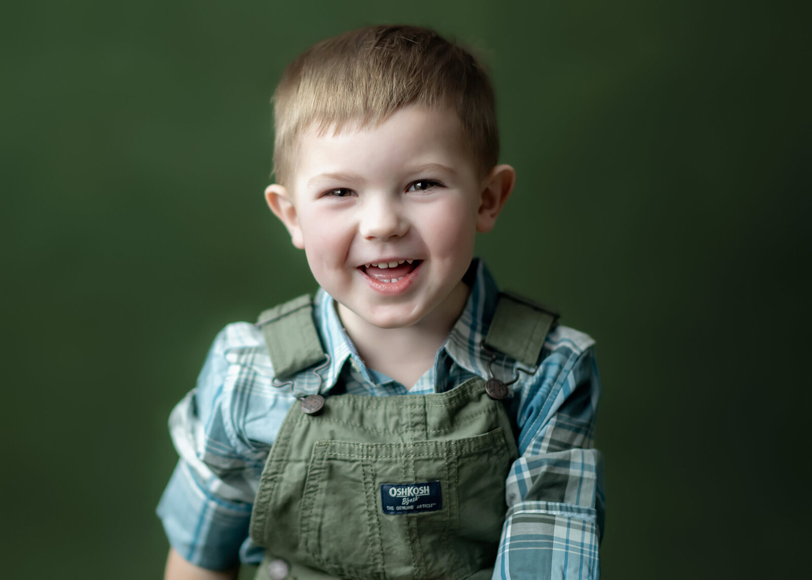 An Iowa Milestone Photographer takes photos of a boy wearing green overalls on a matching green background