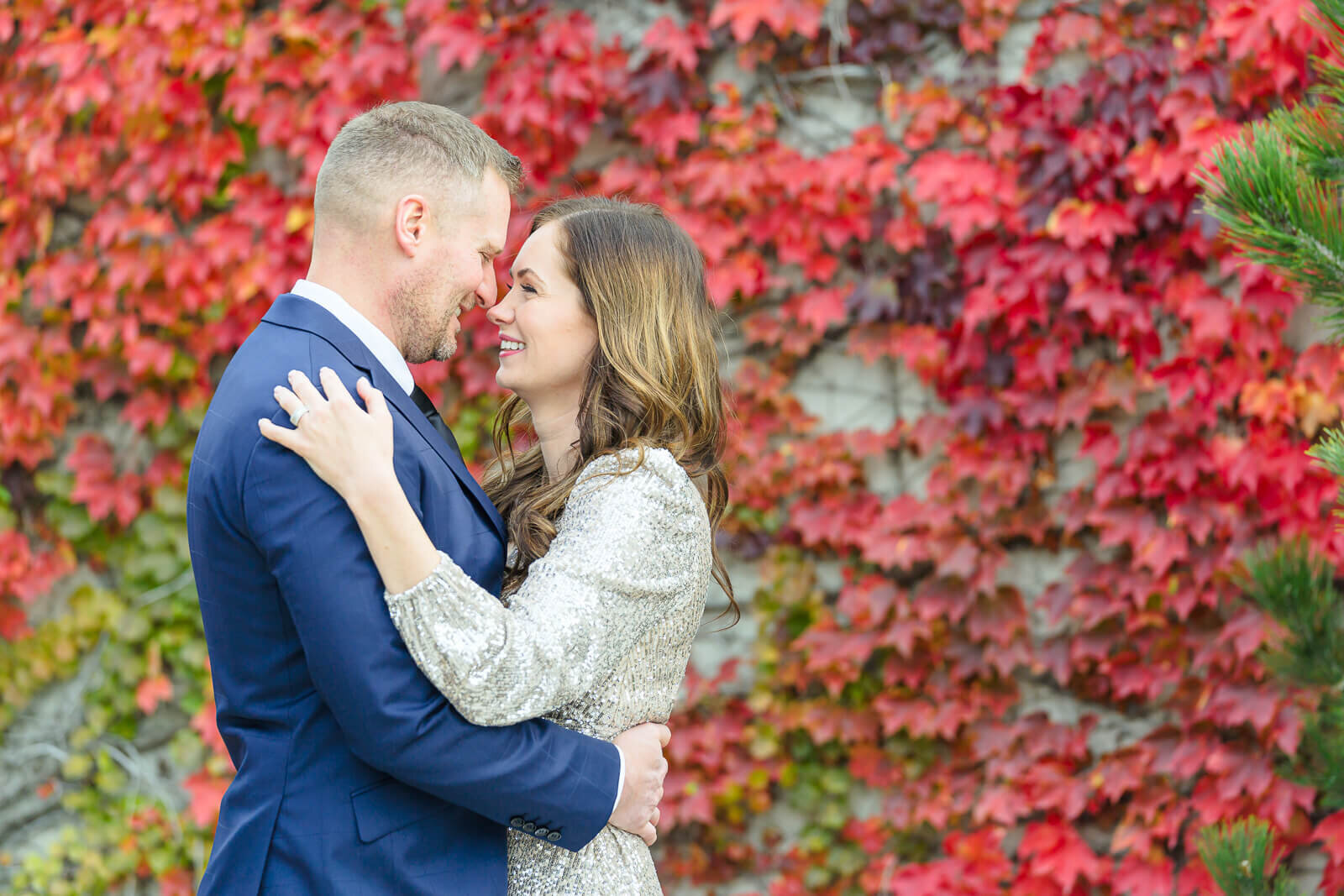 utah engagement photography of an engaged couple smiling at each other in front of vines of vibrant red leaves in the fall