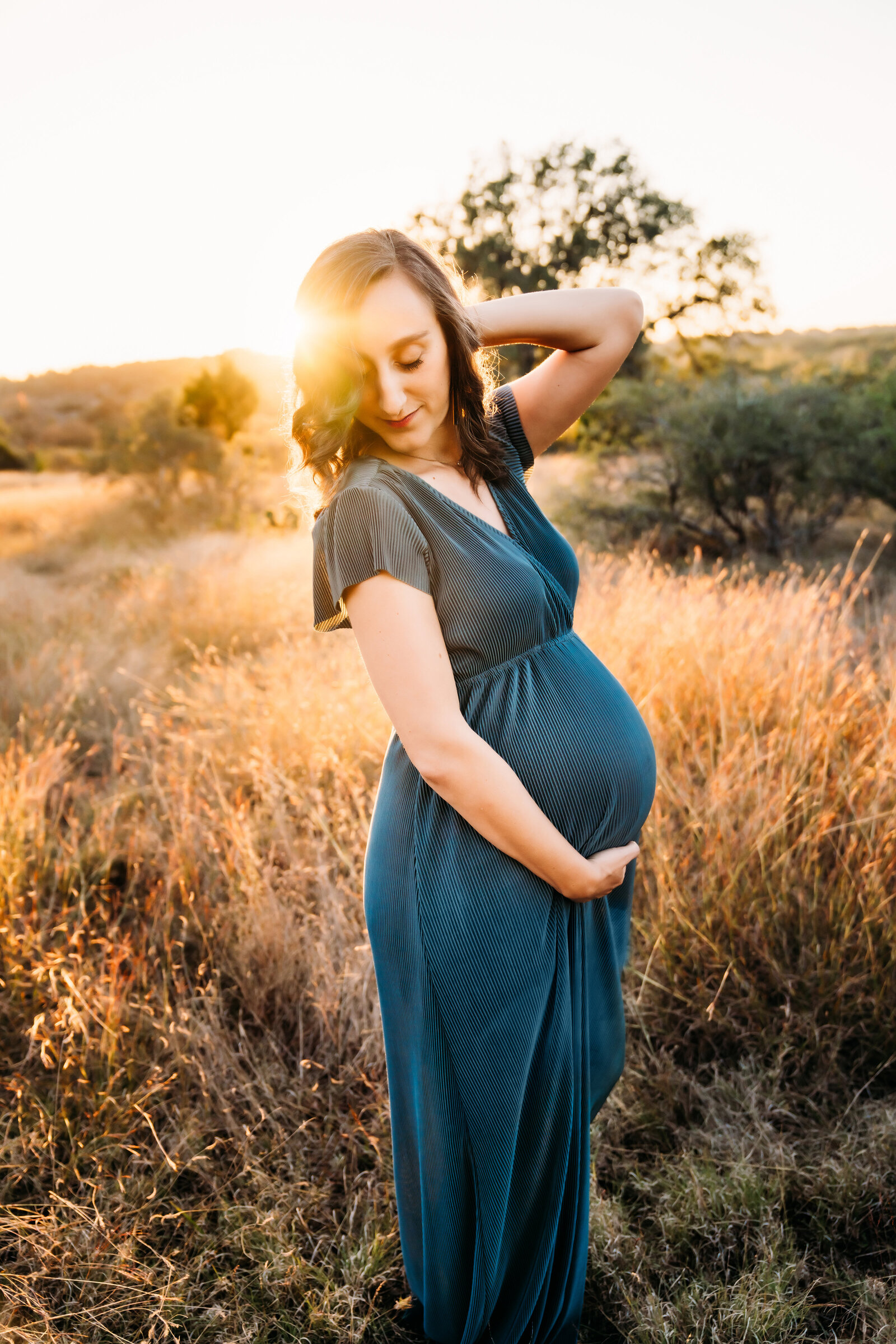 Maternity Photographer, woman in dress feels baby kick as she stands in dry meadow