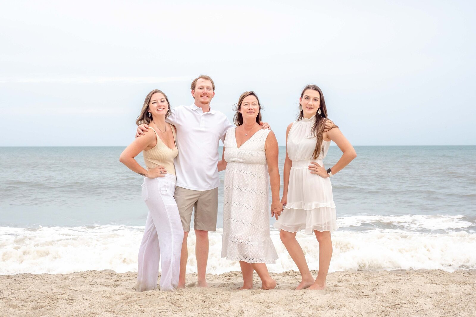  A family of four poses elegantly on Wrightsville Beach, dressed in coordinated white and beige outfits. The gentle waves and serene sky create a peaceful backdrop, ideal for North Carolina family photography, capturing timeless beachside elegance.