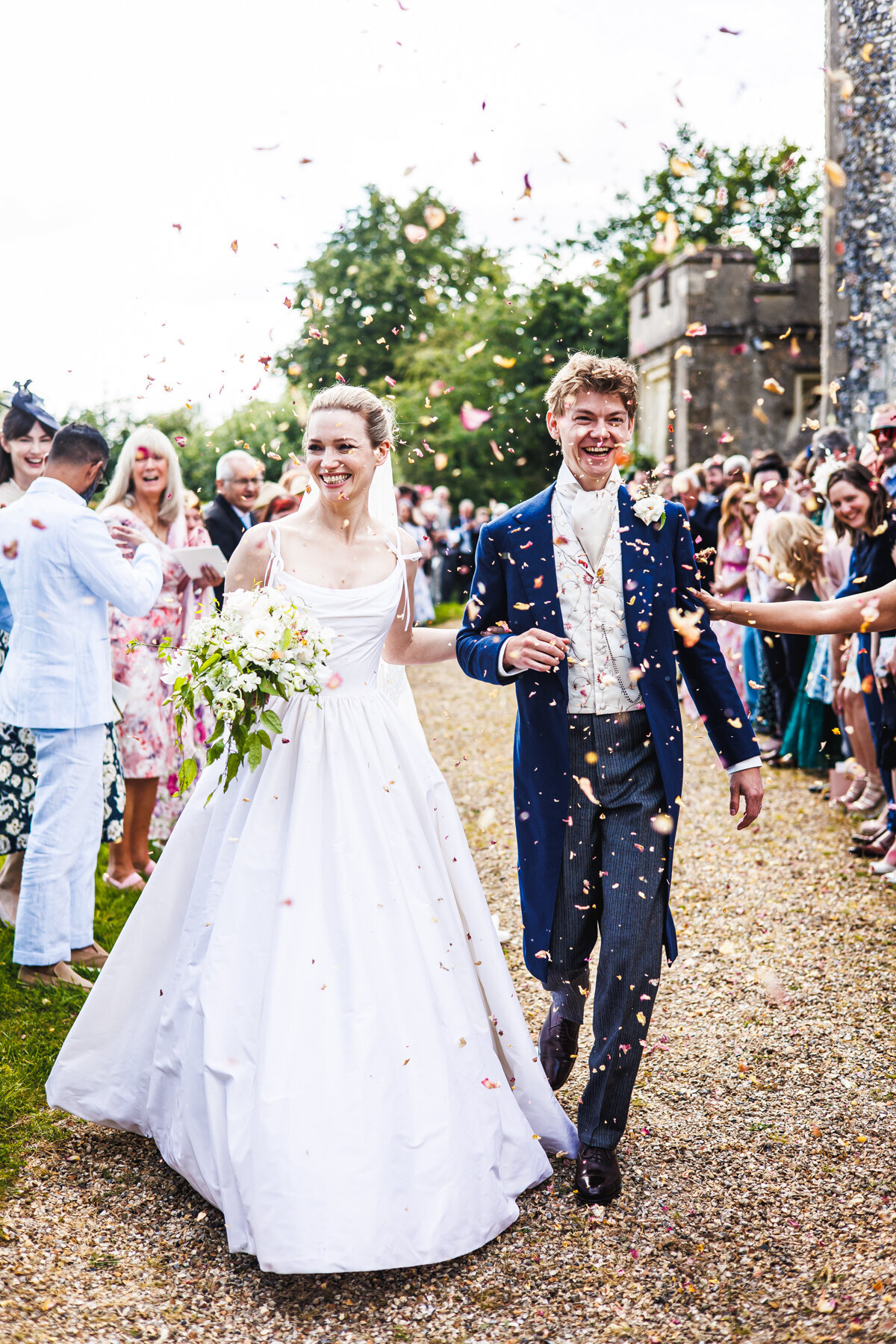 Talulah and Thomas walk hand in hand, smiling at guests as they are showered with confetti at a church wedding