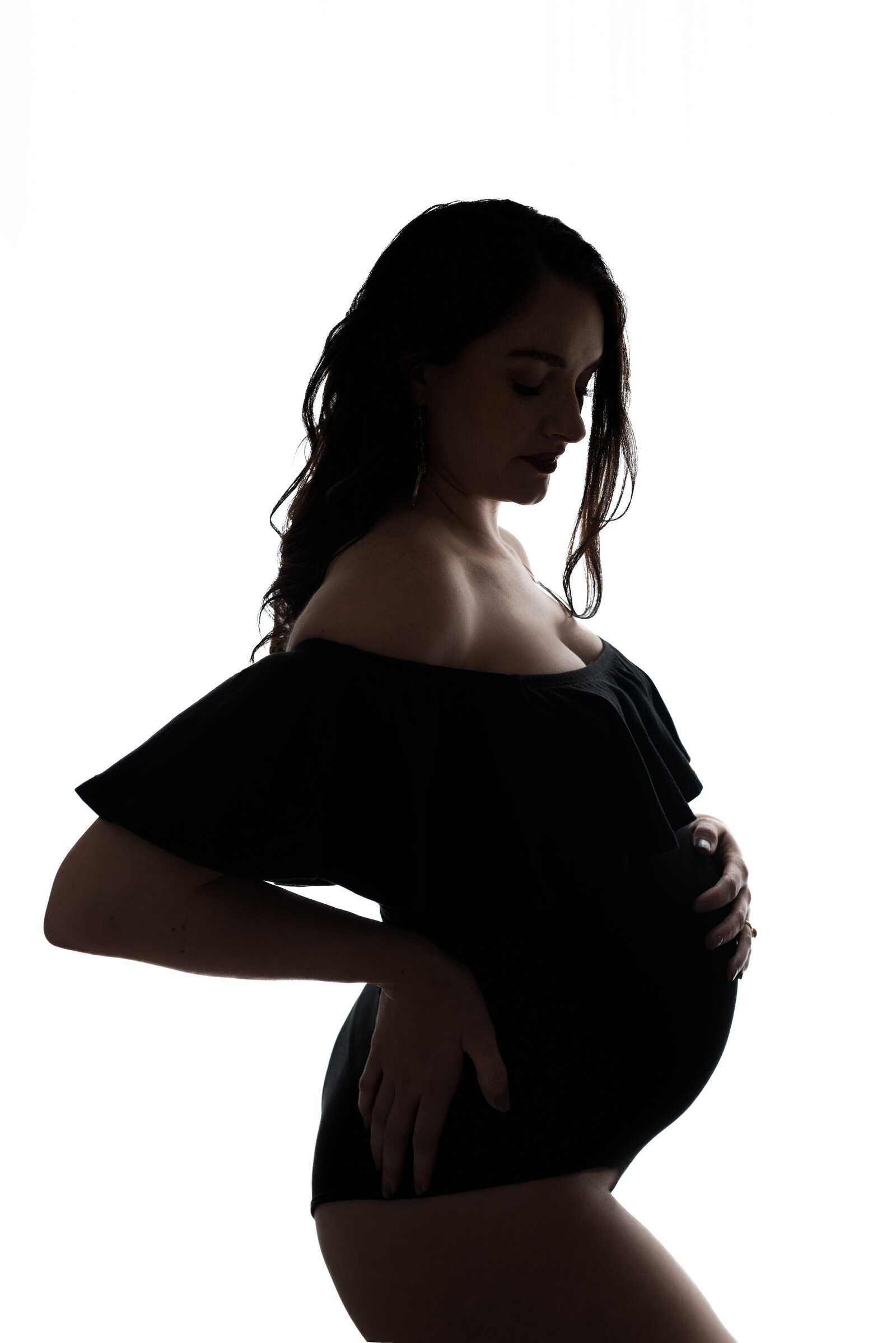 Woman in a black bodysuit poses with her hand on her stomach for her studio maternity pictures in Huntsville Alabama