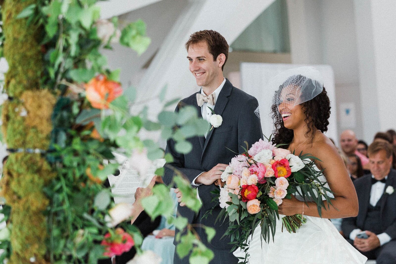 Bride and groom smiling while bride holds bouquet walking down aisle