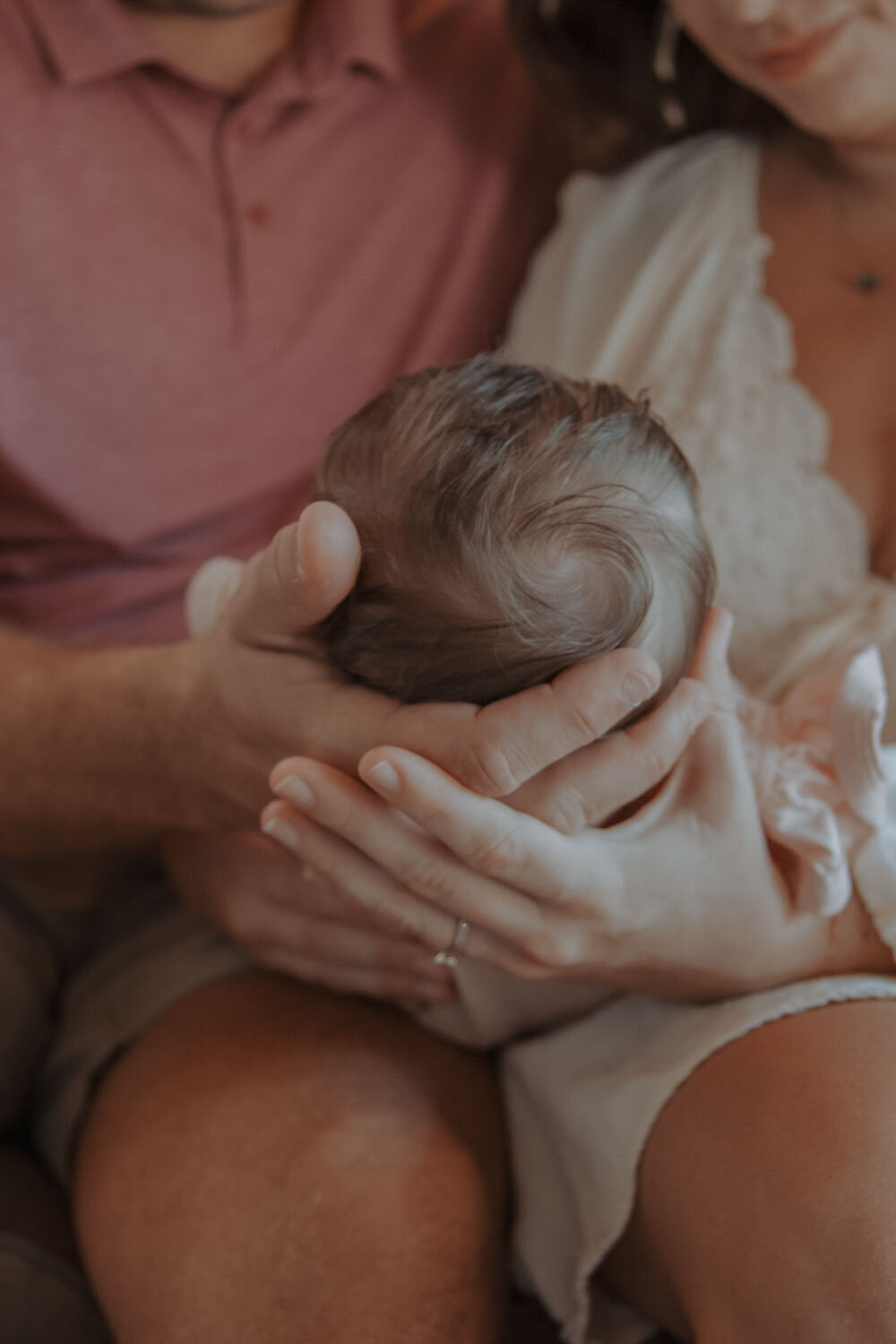 Parents holding their newborn's head gently, a sweet moment of newborn photography