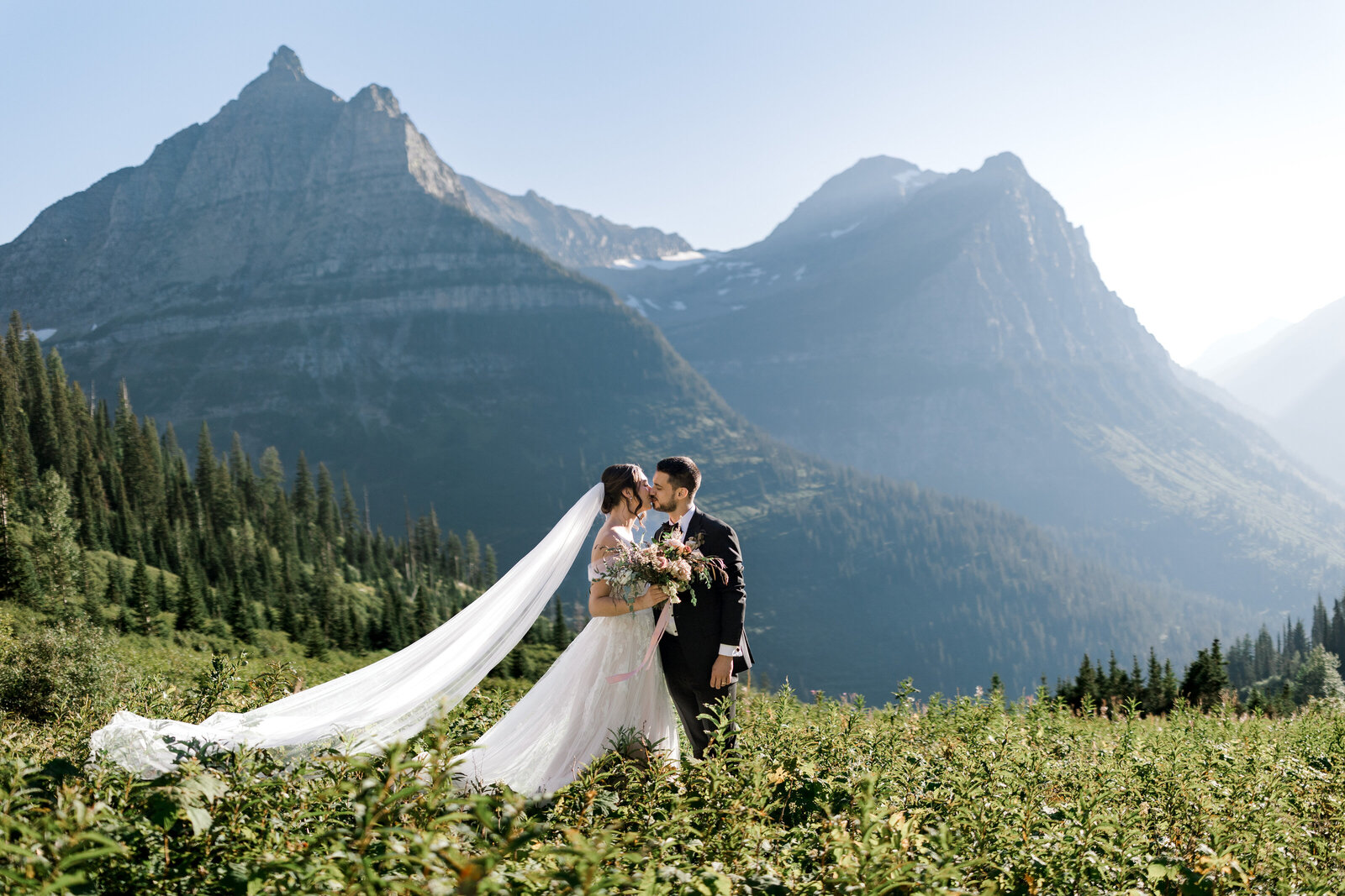 Bride and groom share a kiss in front of the mountains in Glacier National Park