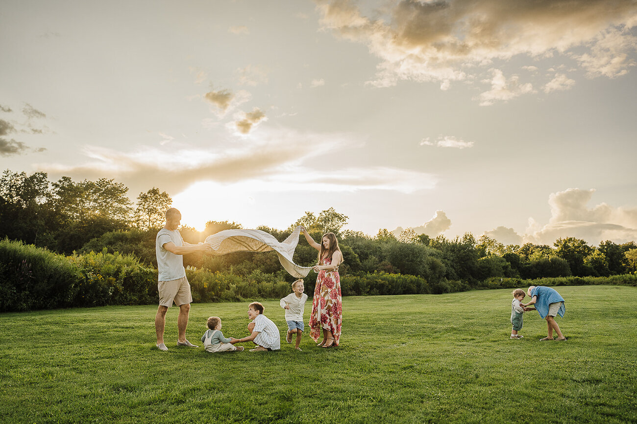 family with five sons frolick in field at sunset