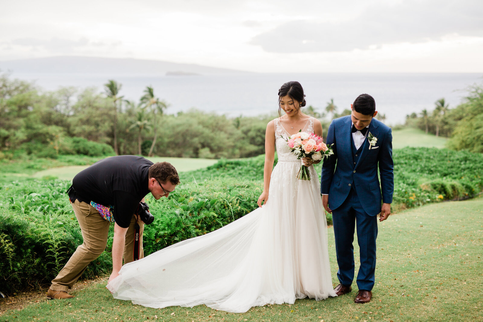 wedding photographer wearnig a black shirt and khakis fixes a brides dress