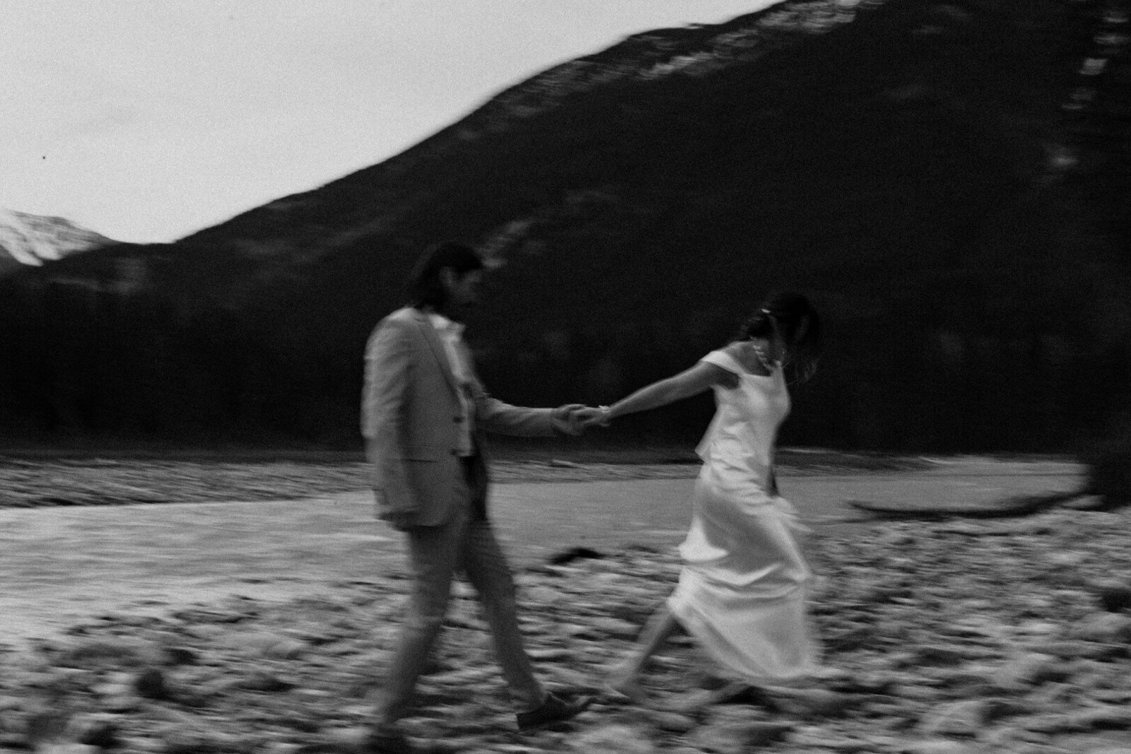 bride and groom walking on rocks by a river in canada holding hands