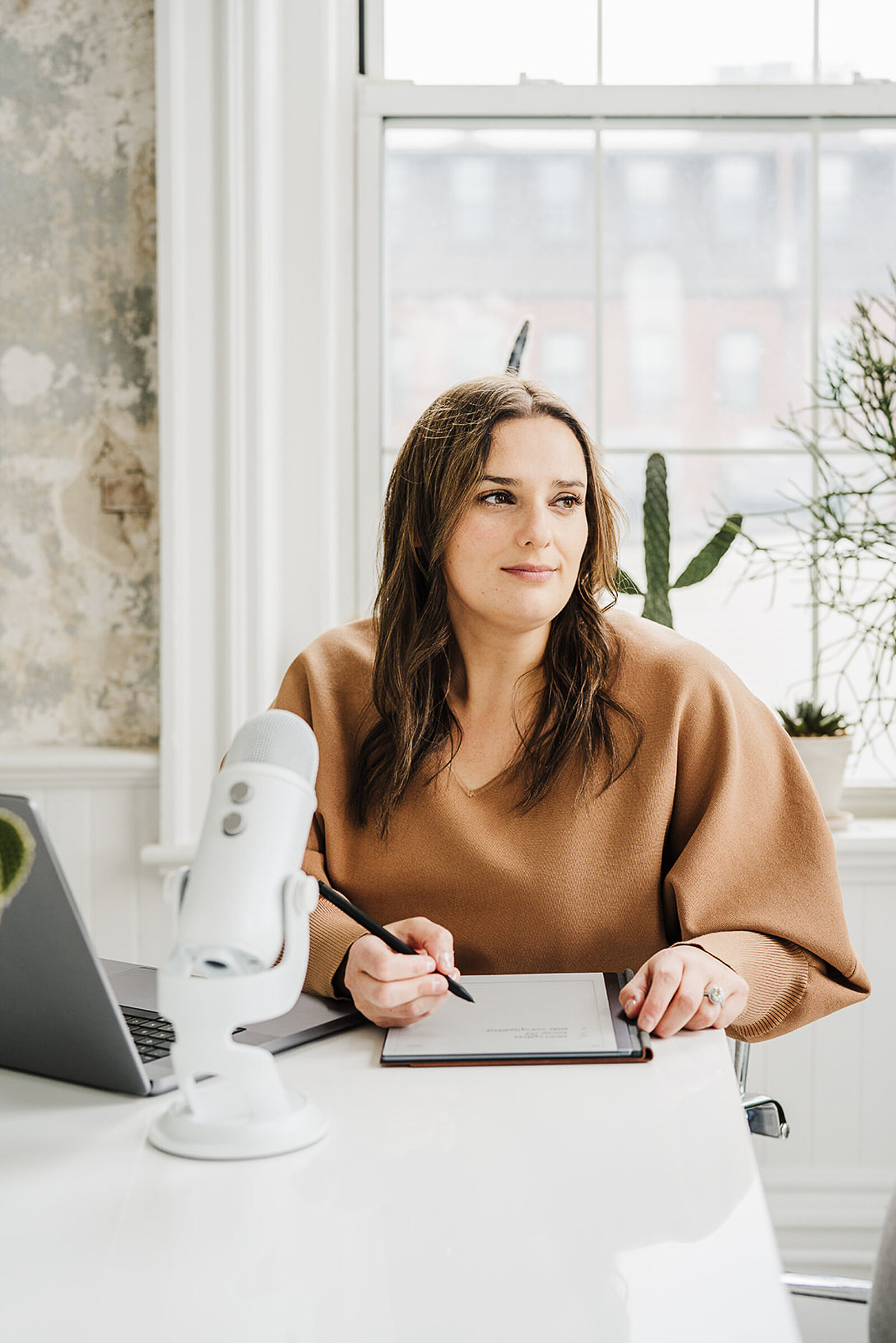 woman stares out of window while writing in notebook